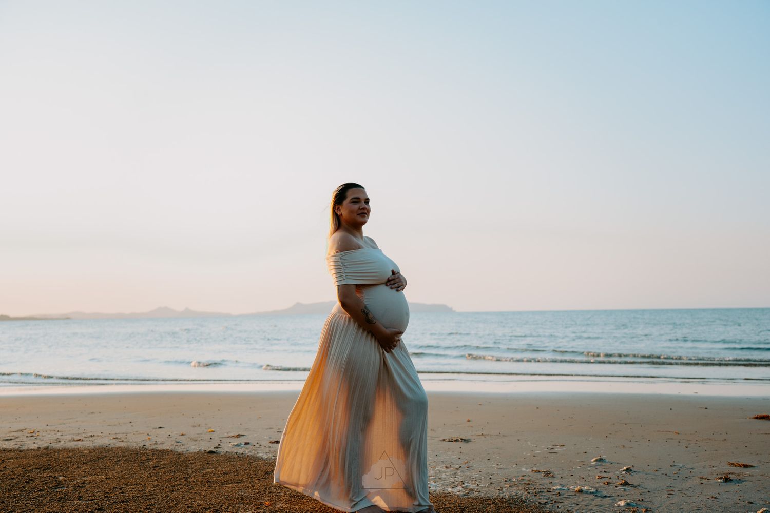 Couple embraces on a serene beach at sunset with soft pastel colors in the sky.