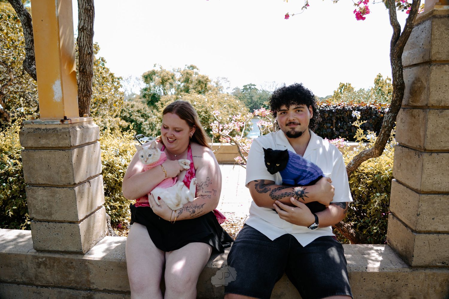 People sit and relax together on stone benches in a sunny outdoor garden setting.