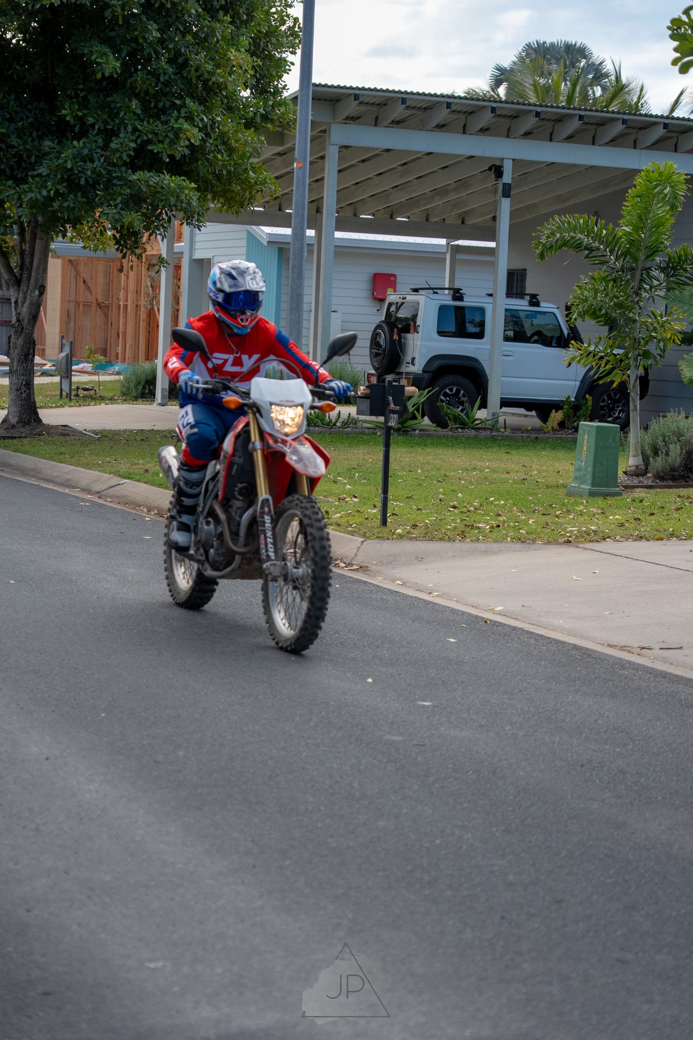 A sequence of shots showing a red off-road motorcycle from different angles parked in a residential driveway.