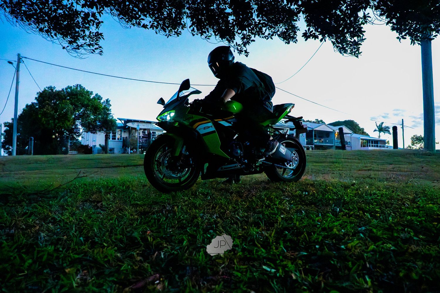 A motorcycle rider leans into a curve on a country road with farm fields in the background.