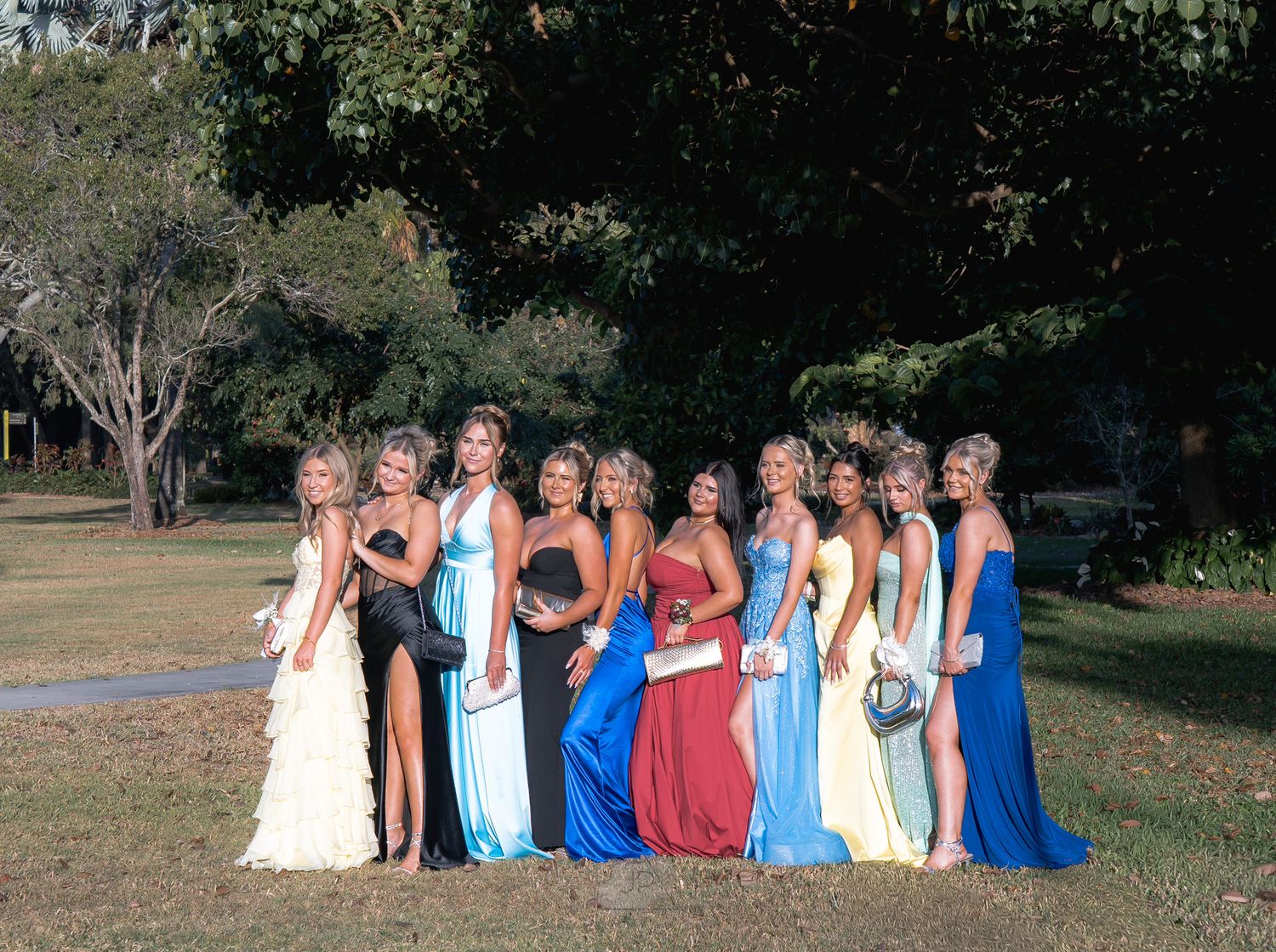 Group of friends in colorful dresses gather outdoors for summer photos in a park setting.