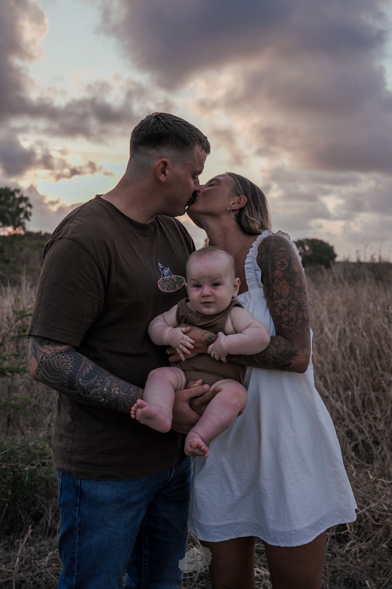 Family shares tender moments together during golden hour photoshoot in a rustic field at sunset.