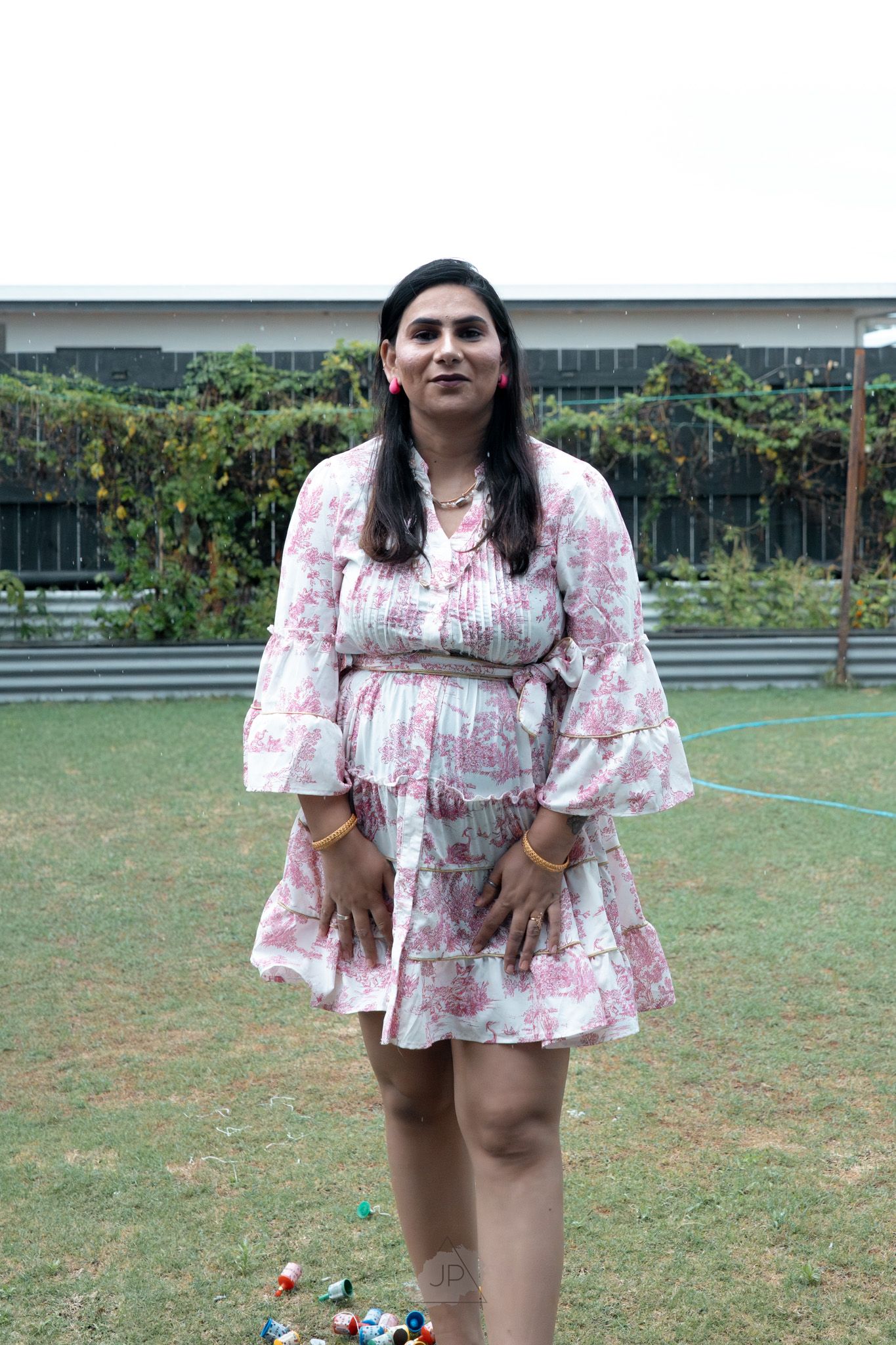 A person in a floral print dress poses outdoors on a grassy field.