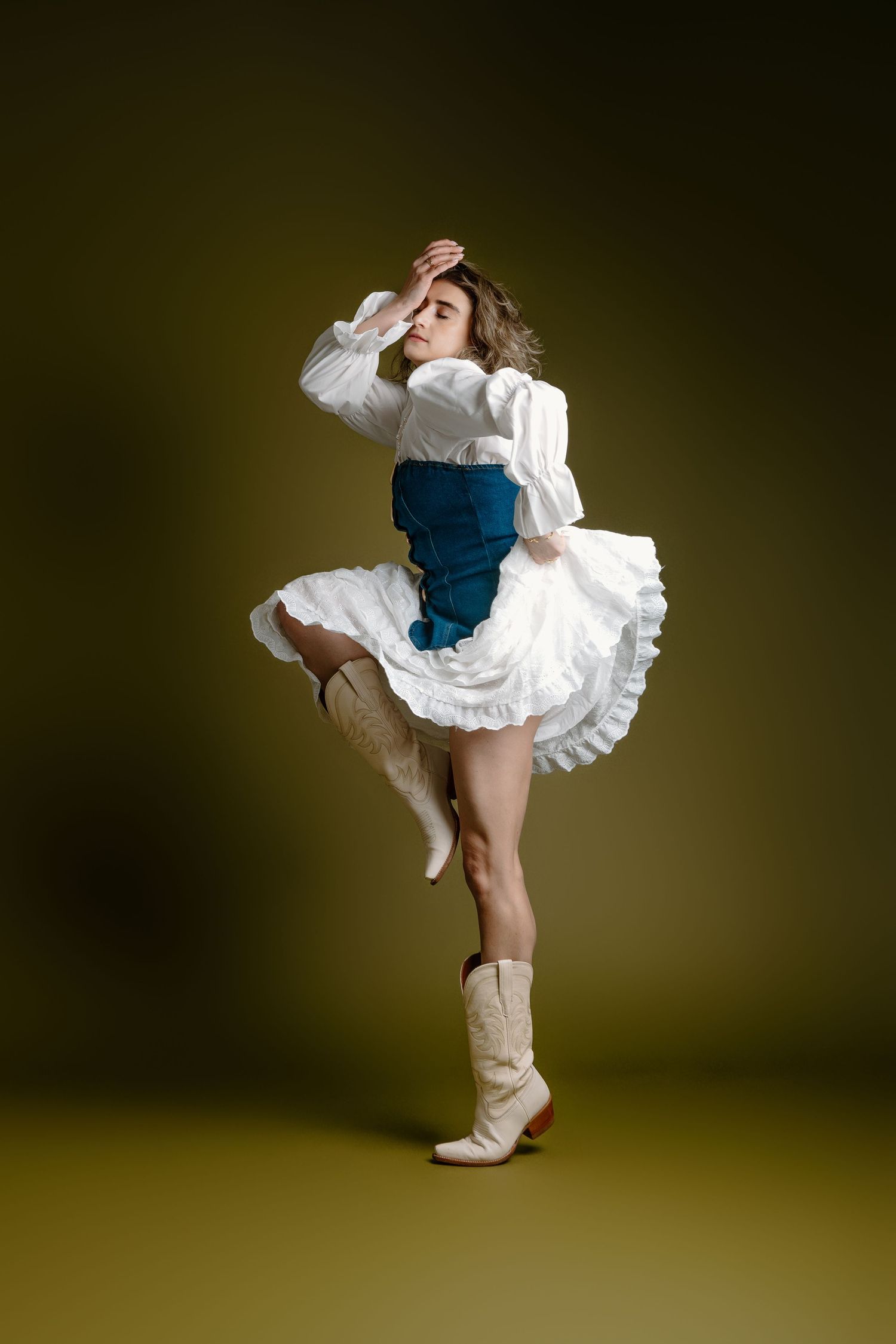 A dancer in a white petticoat and blue costume performs a high-energy kick sequence against a dark background.