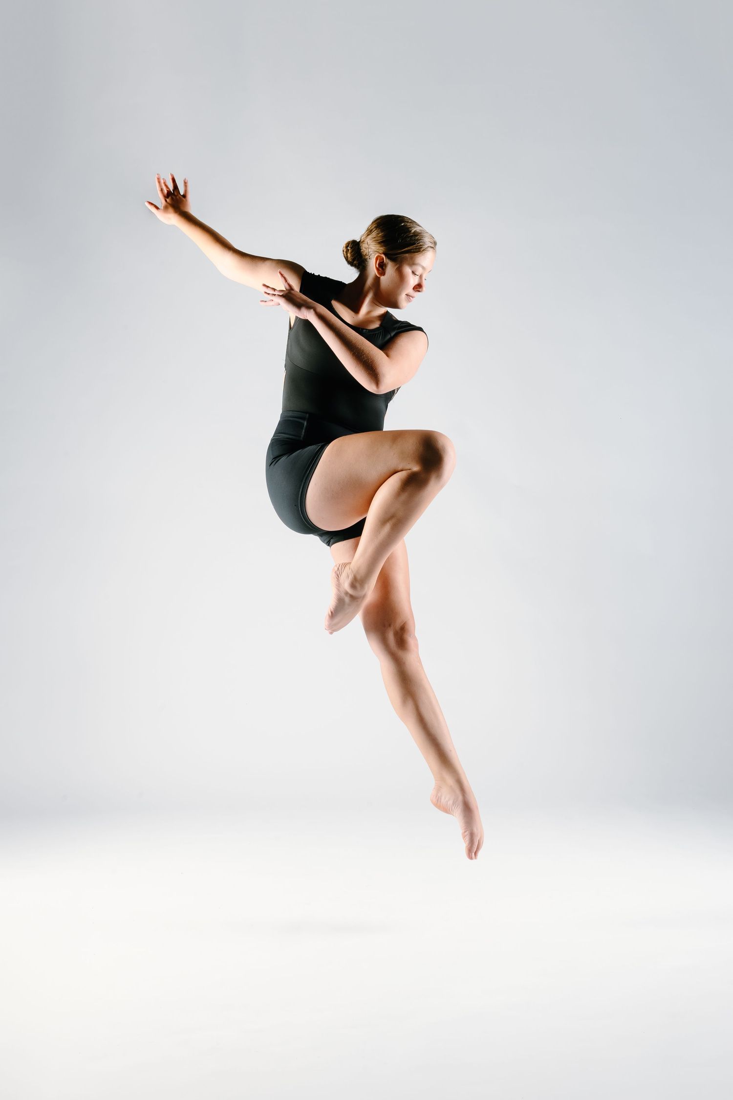 Contemporary ballet dancer in black leotard performs graceful aerial jump sequence on white background.