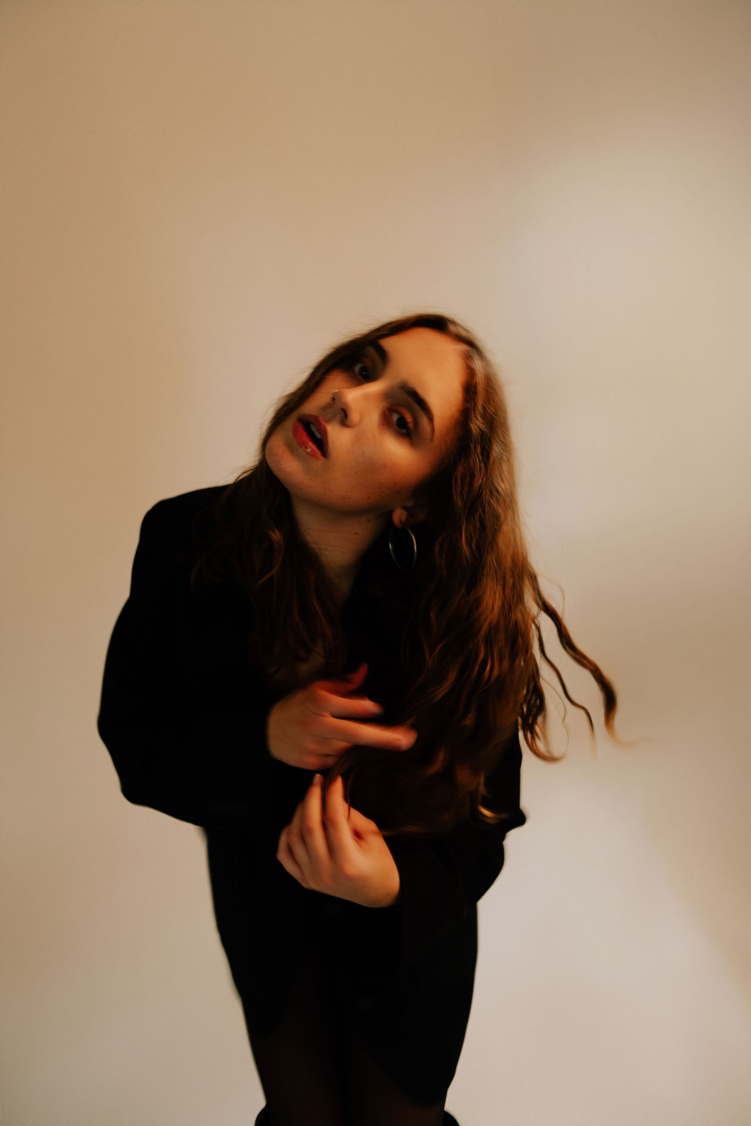 Young woman in black outfit posing against white background with dramatic makeup and flowing hair.