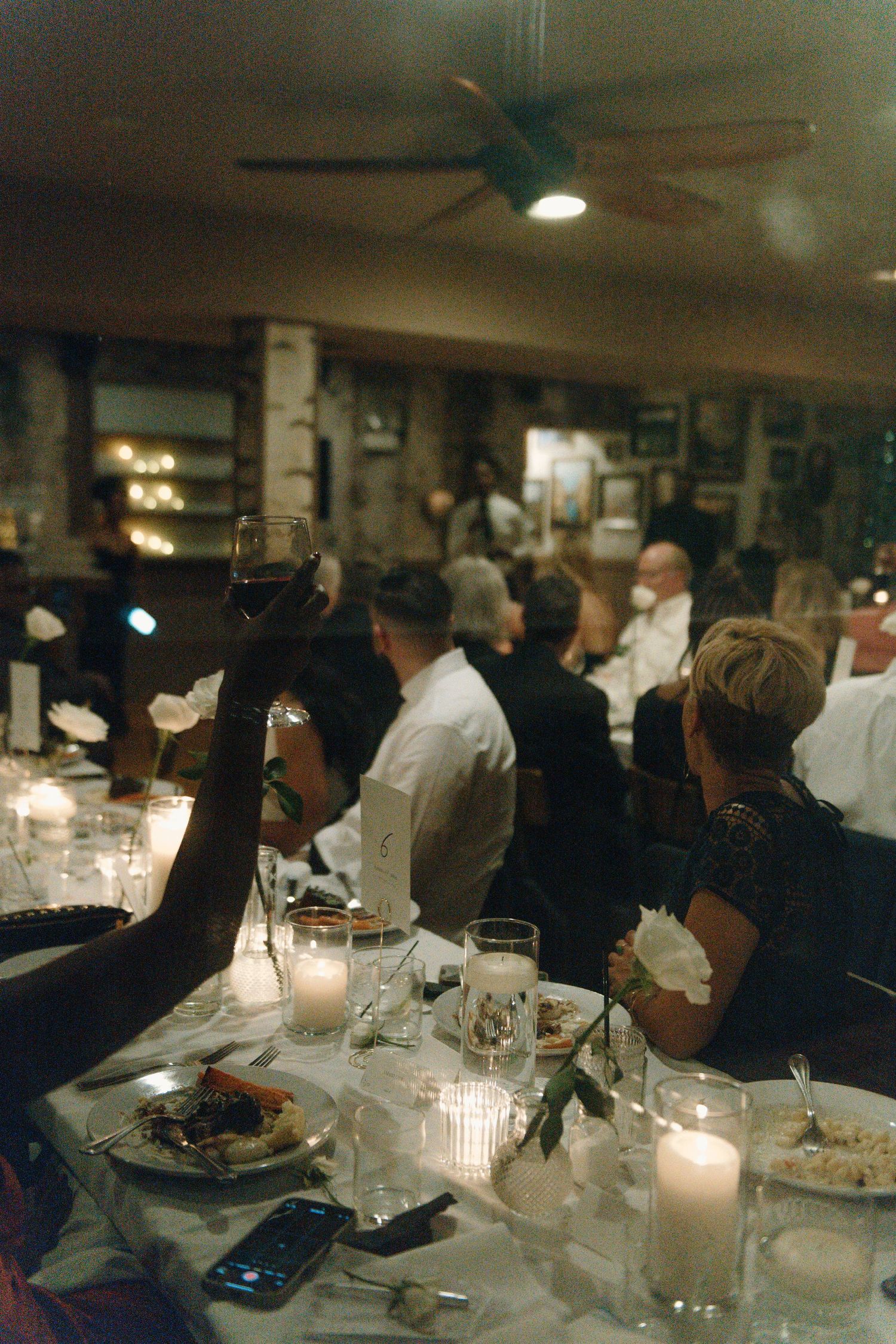 A dimly lit restaurant dining room with candles on tables and people gathered for a formal dinner event.