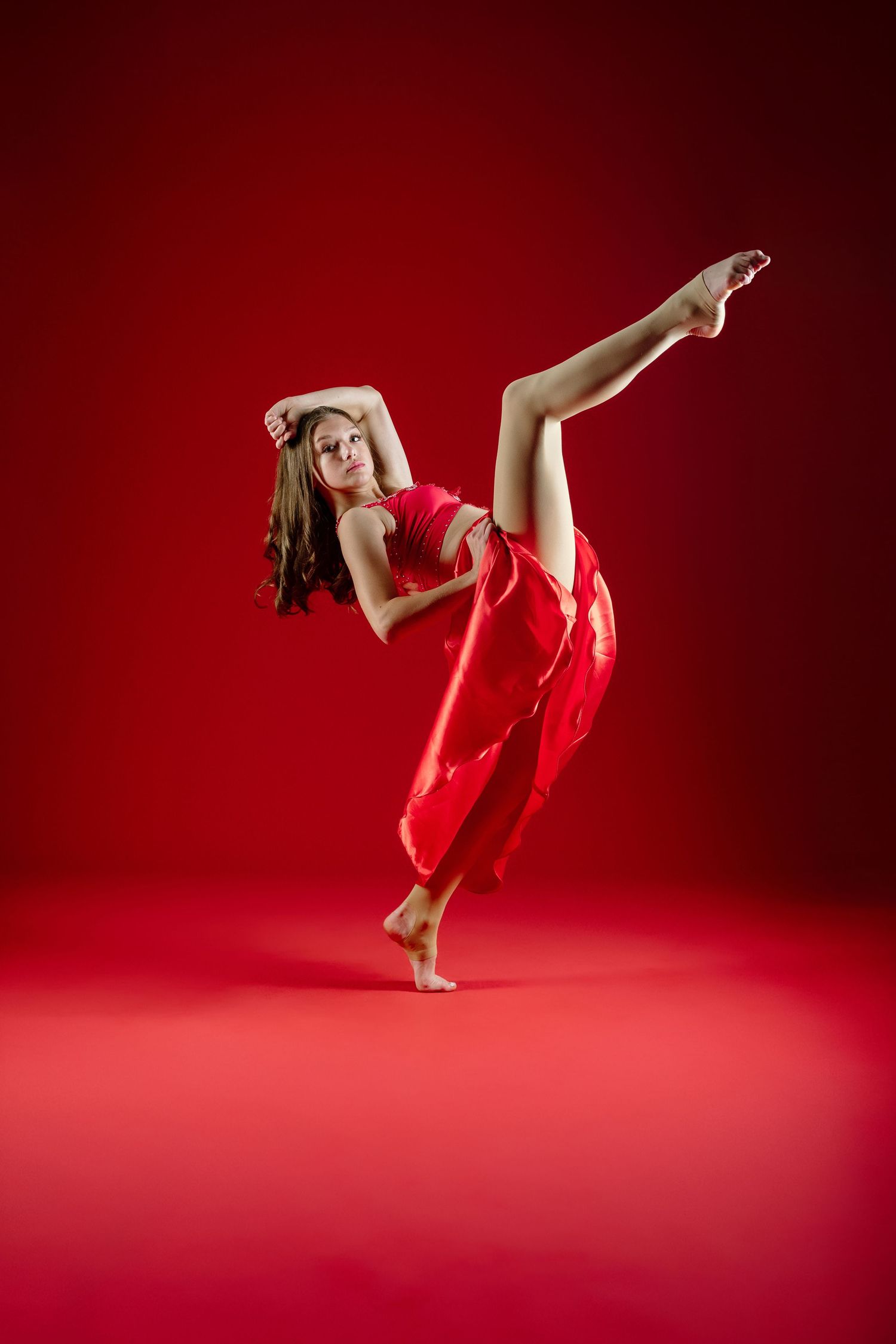 Dancer in flowing red dress performs dynamic contemporary dance movements against a deep crimson background.