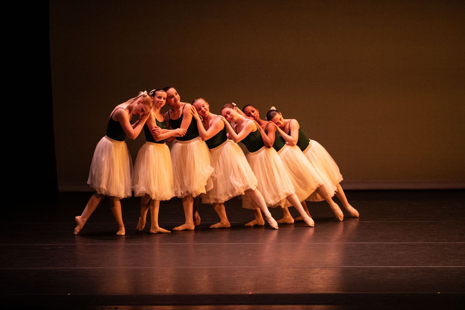 Ballet dancers in white tutus perform a synchronized dance routine on a dimly lit stage during a performance.