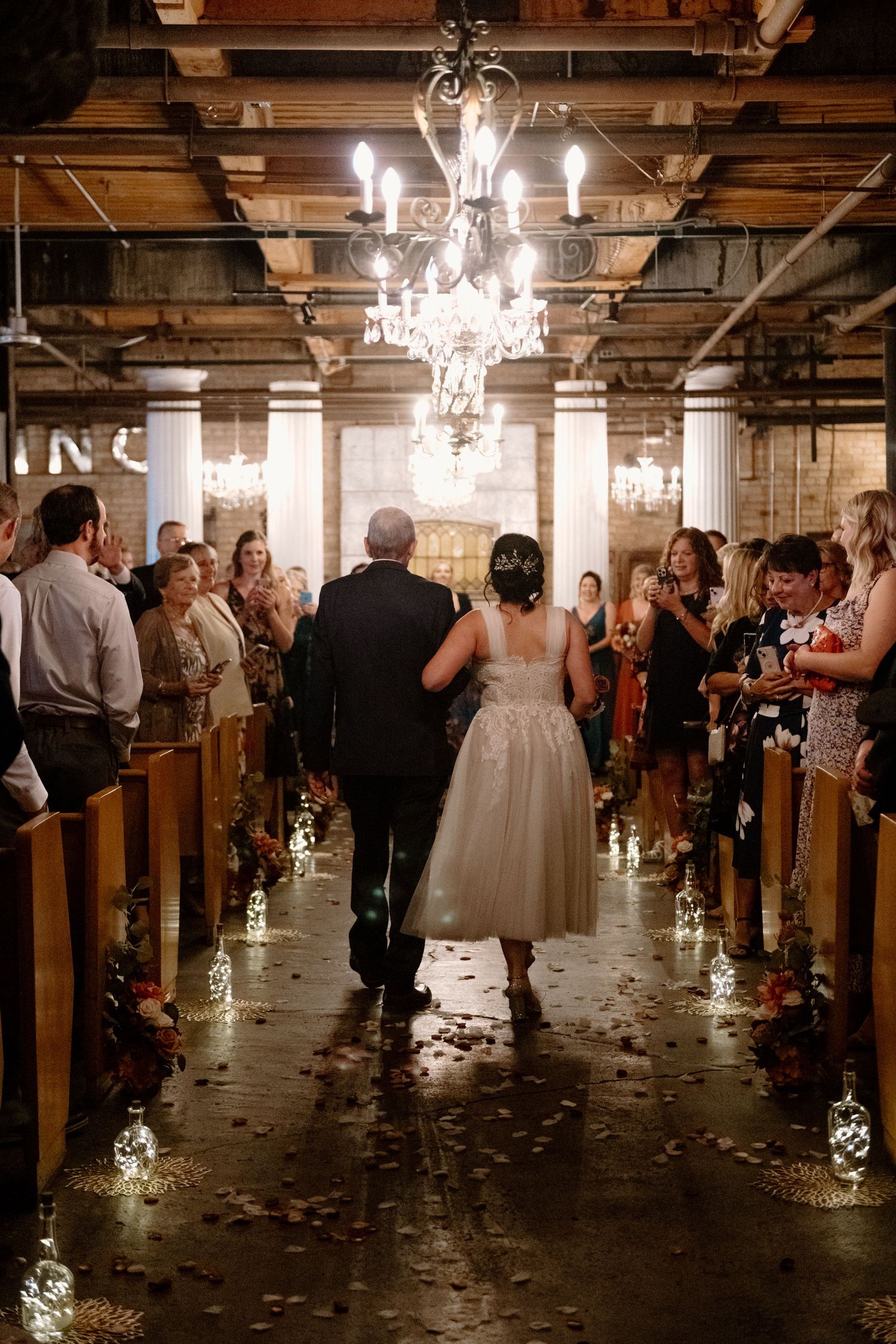 Wedding guests dance and celebrate in a rustic venue with elegant chandeliers and wooden church pews.