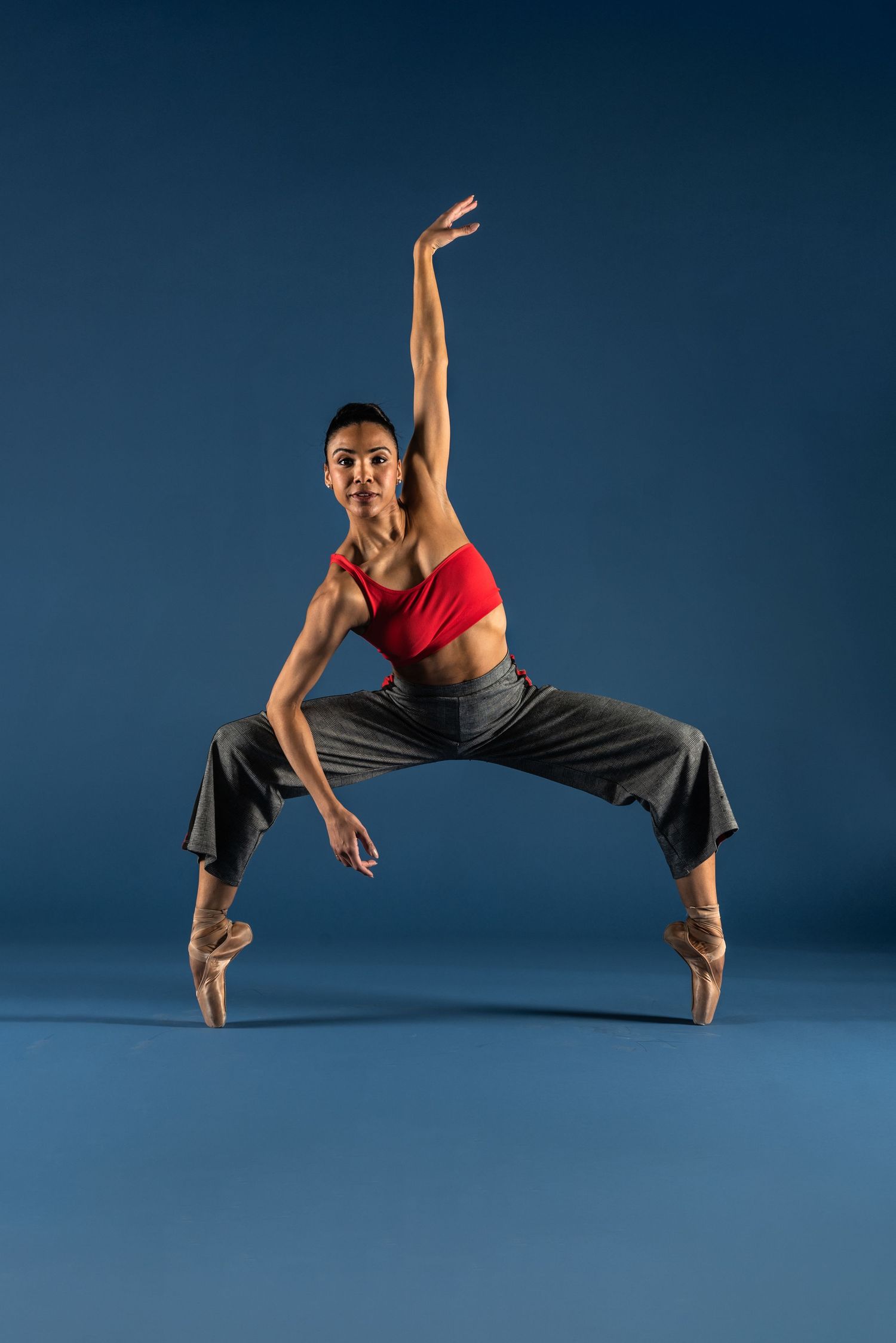 A modern dancer performs a dramatic side-tilting movement sequence against a dark blue backdrop.