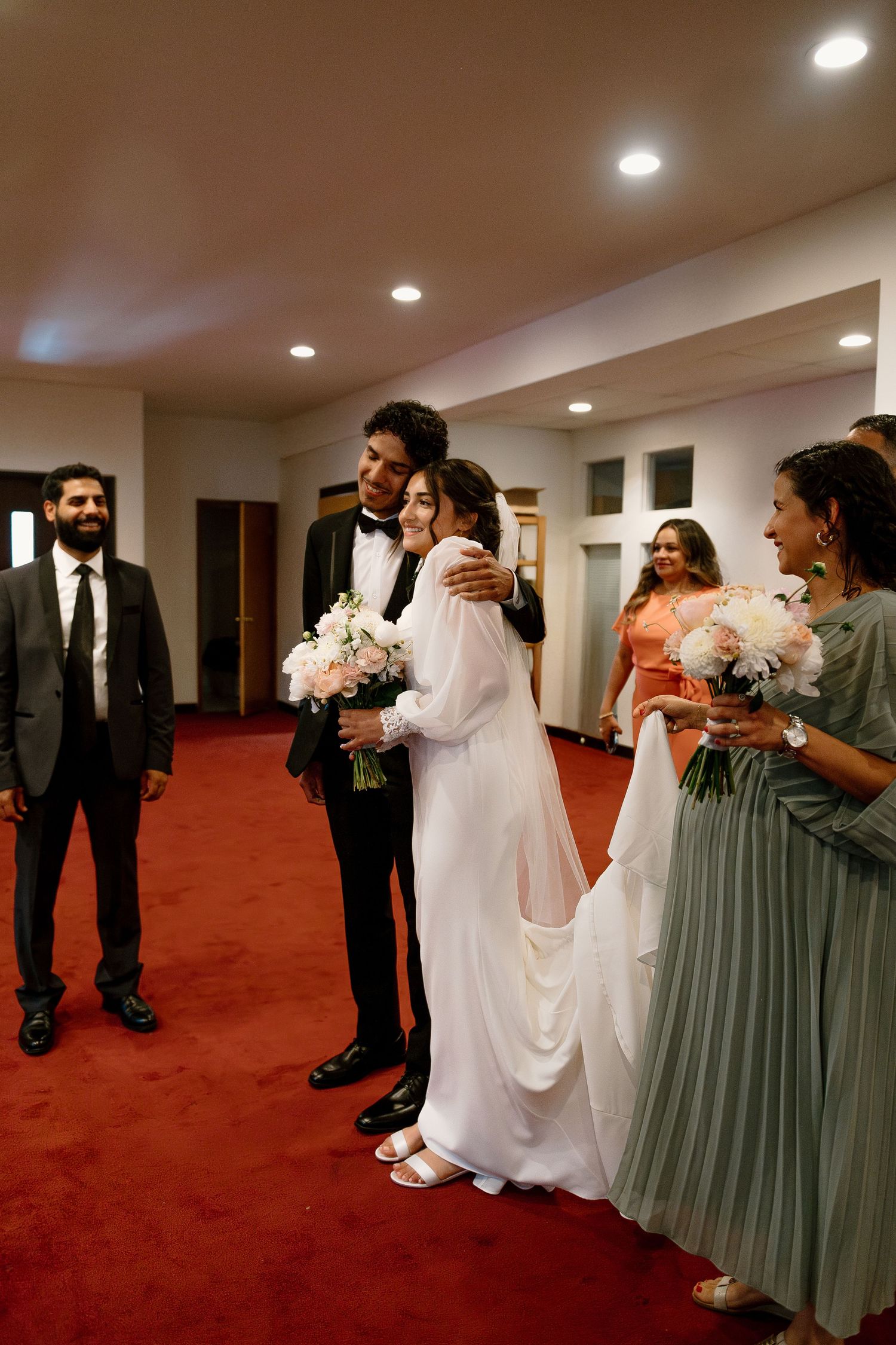 A wedding party poses in a corridor with red carpeting and recessed lighting.