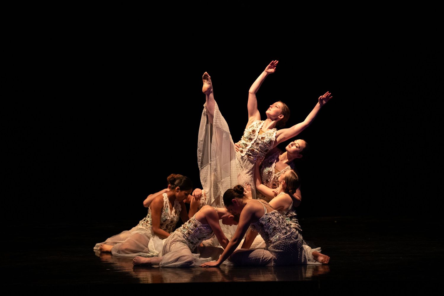 Dancers perform an elegant contemporary piece on stage with dramatic lighting and flowing costumes.