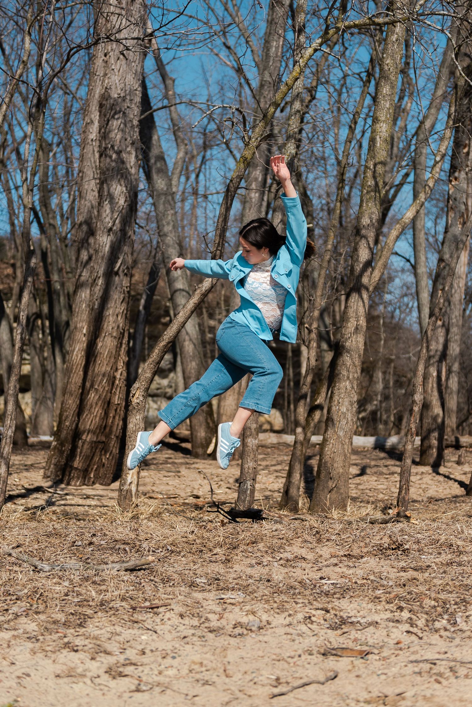 A person in turquoise outfit does aerial dance moves in a sequence across wooded terrain on a sunny day.