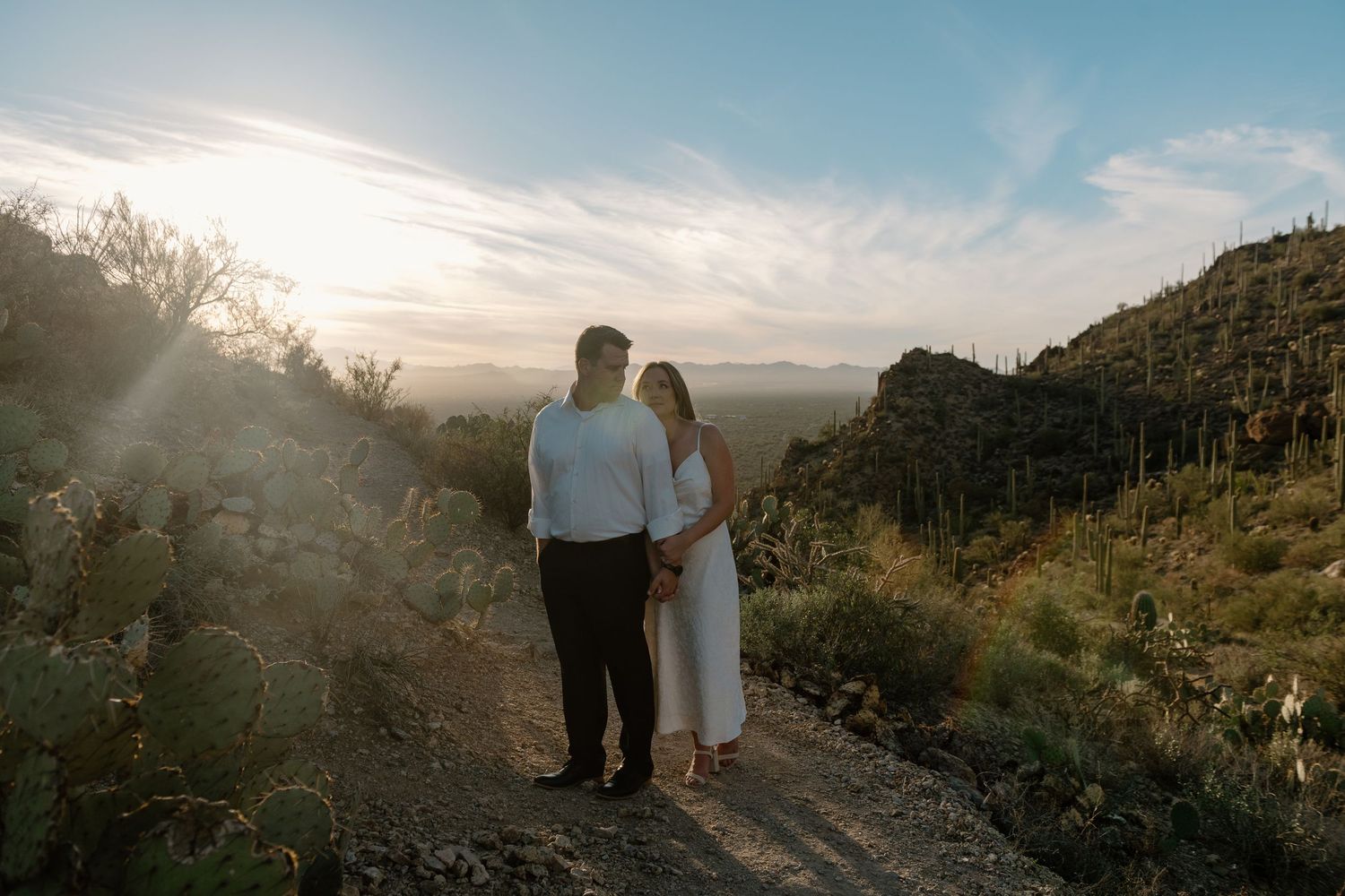 Couple stands on mountain trail overlooking desert landscape at sunset in Saguaro National Park.