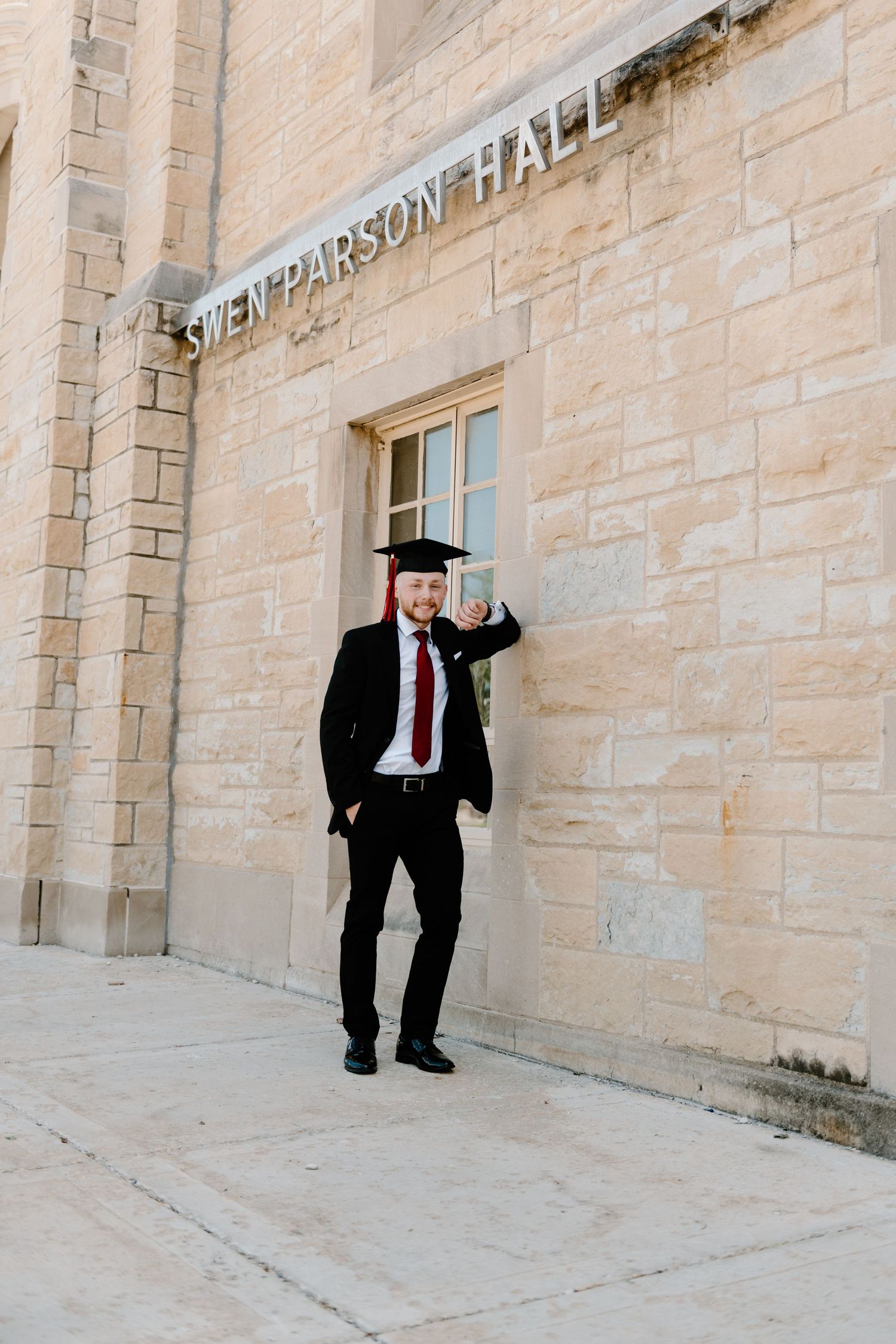 graduate Man in black suit and red tie performing comical poses against a beige stone wall at three different angles.