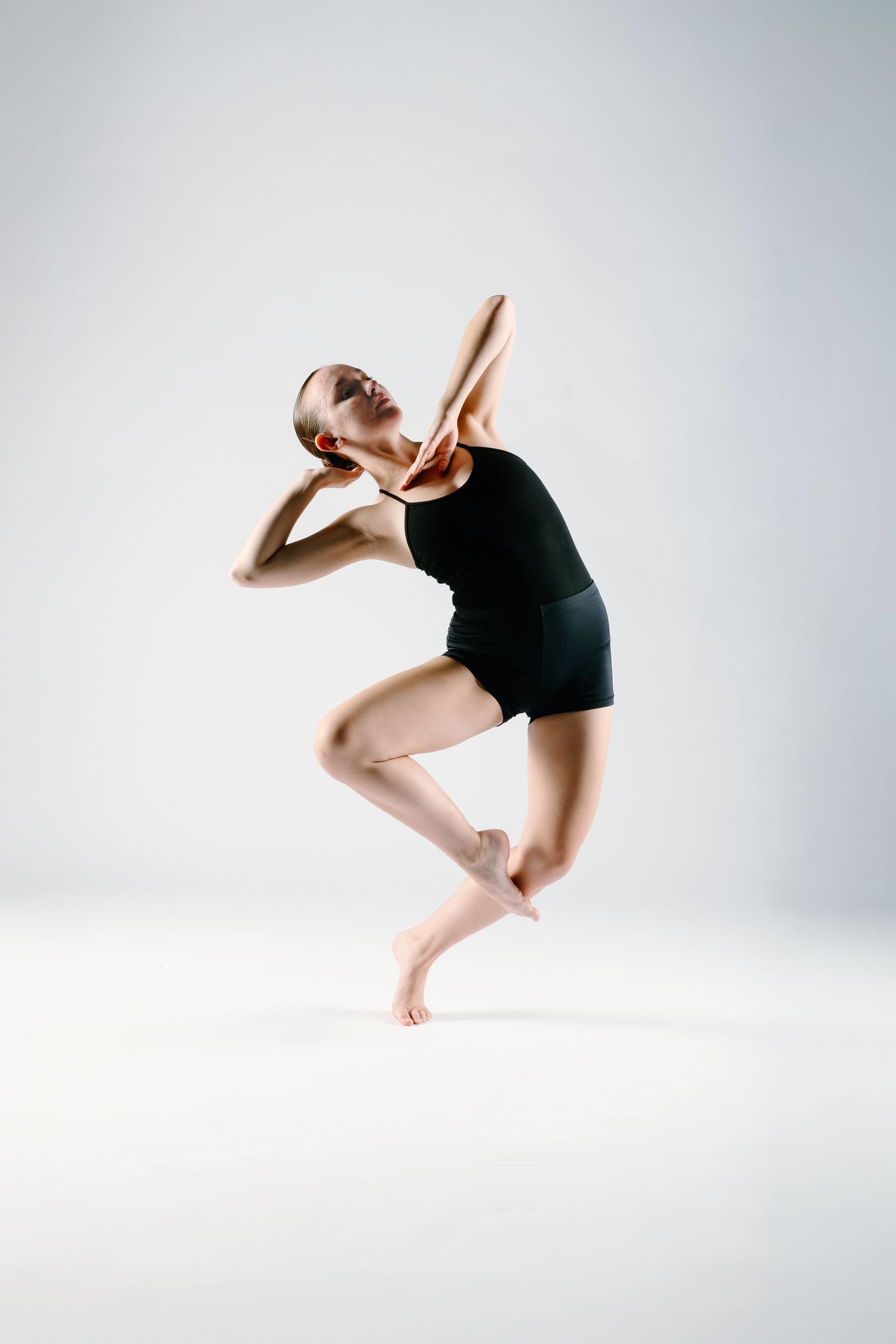 Contemporary dancer in black leotard performs graceful movement against white background.