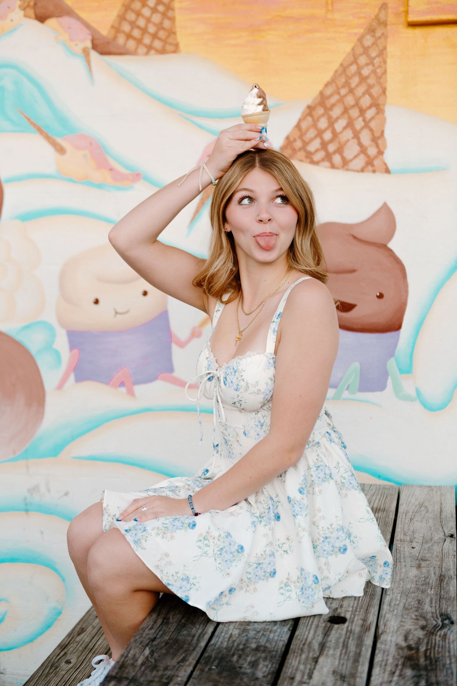 A person in a floral summer dress poses playfully in front of a colorful ice cream themed mural.