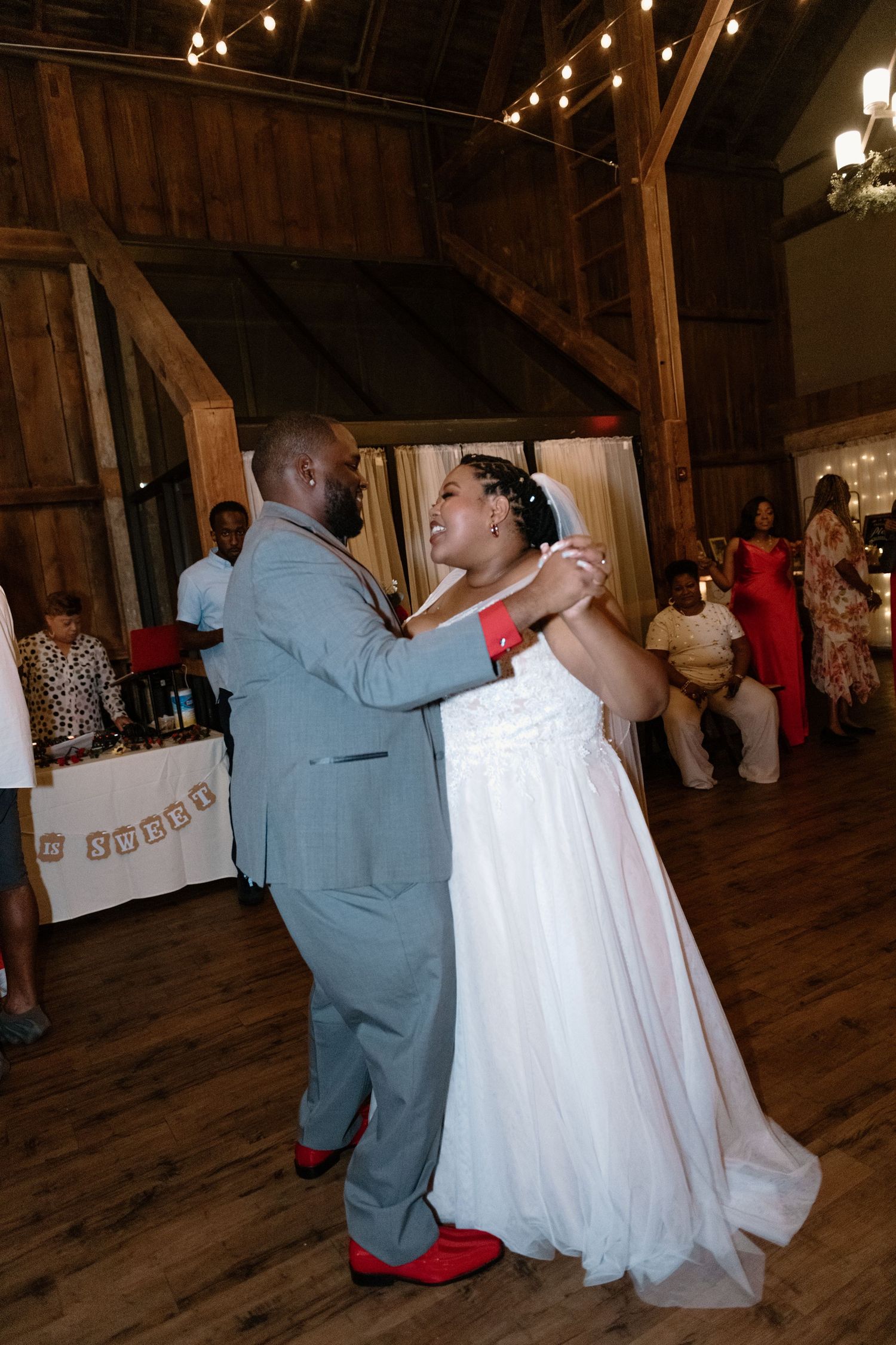 A couple shares their first dance as newlyweds in a rustic barn venue with string lights overhead.