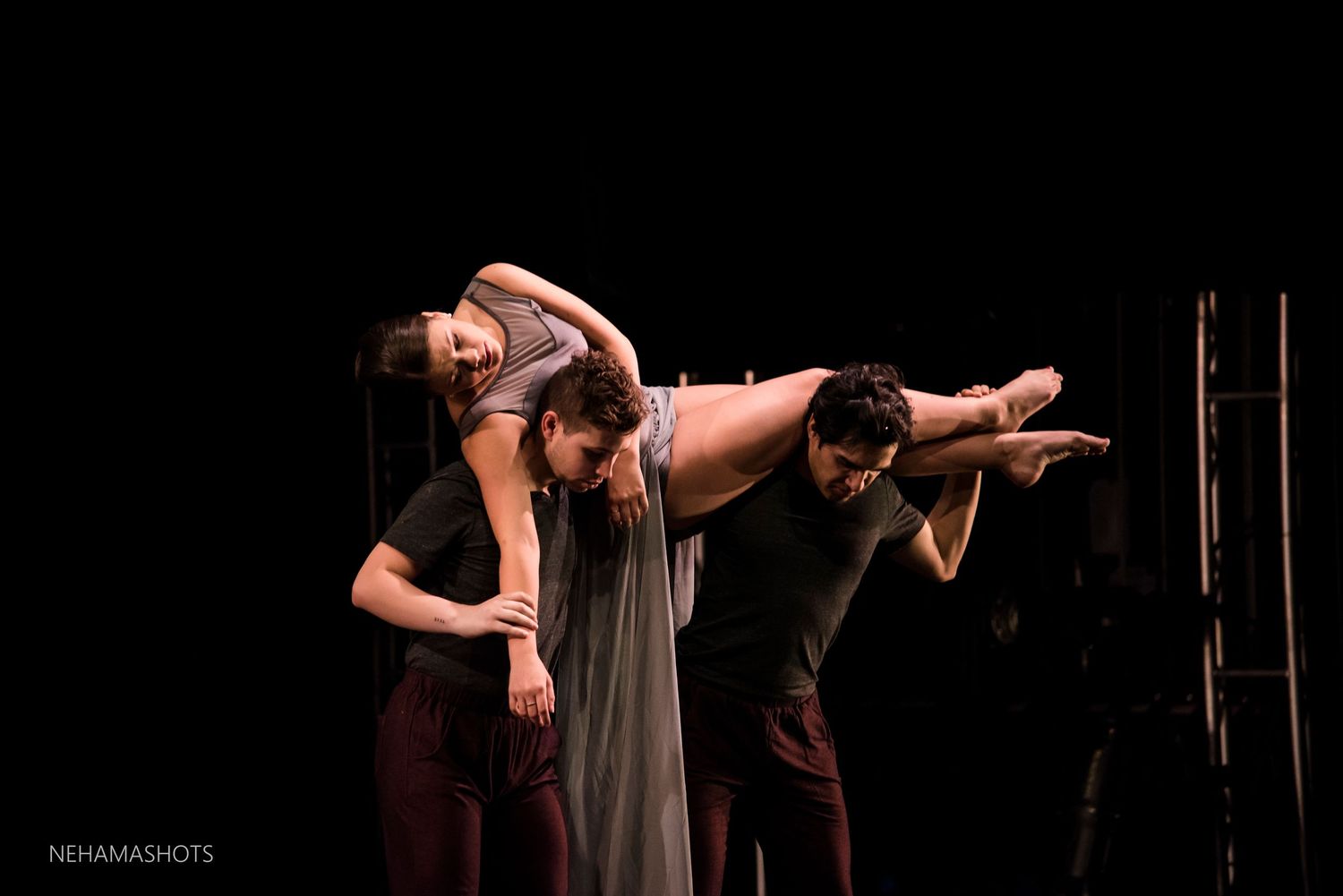 Modern dancers perform an expressive duet with graceful arm movements on a darkened stage.