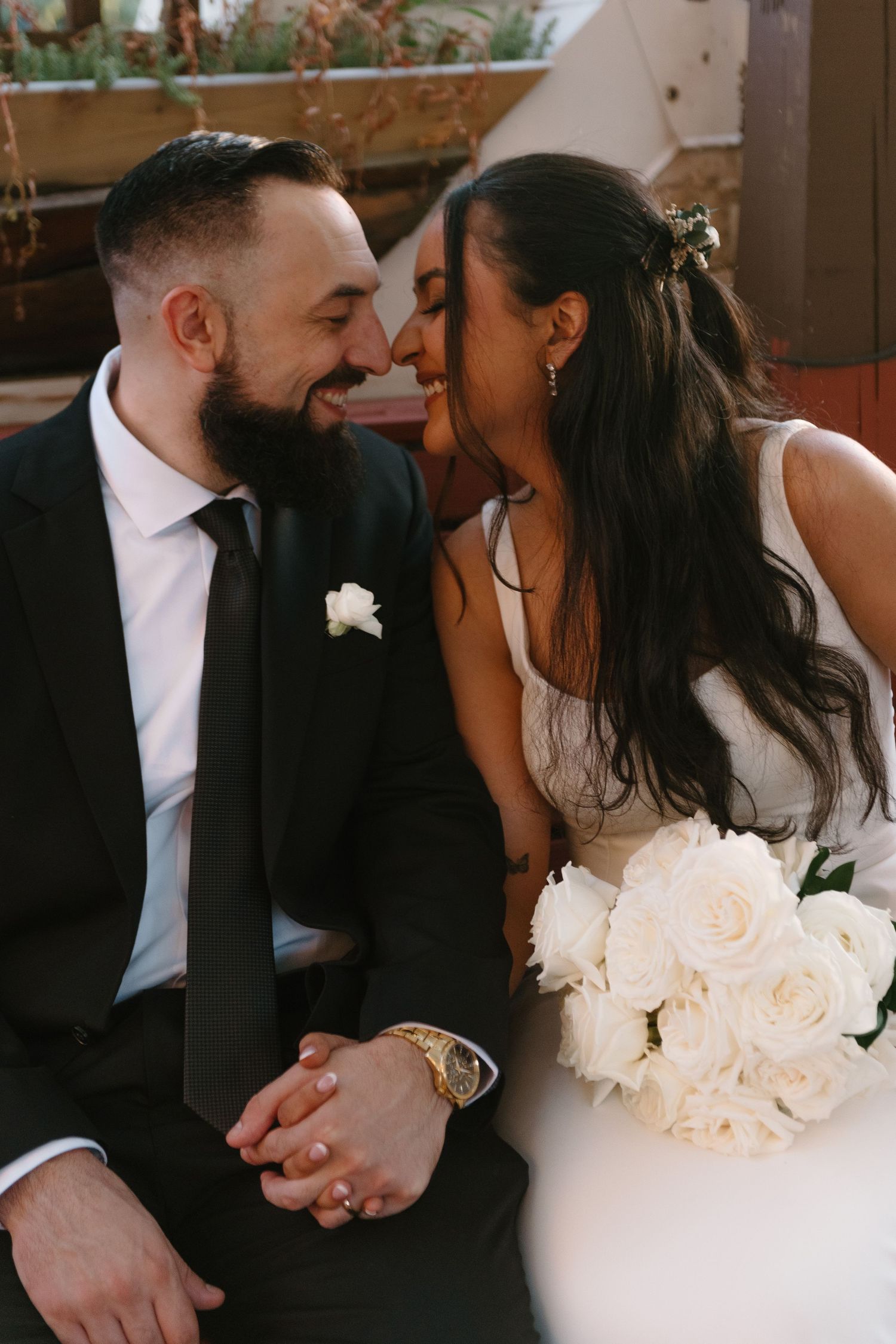 A romantic wedding moment captured as newlyweds share an intimate laugh while holding a bouquet of white roses.
