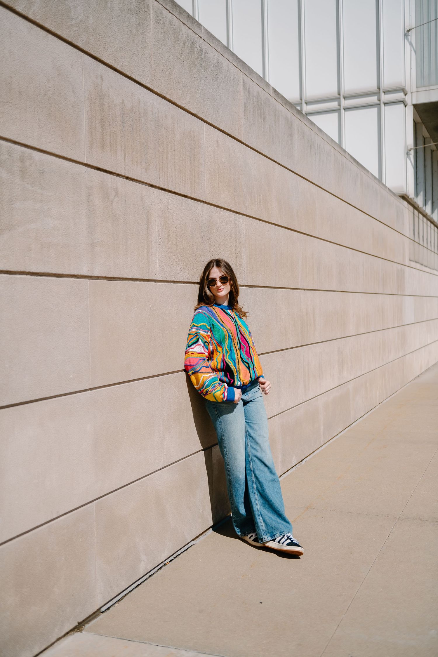 Person in blue clothing sits against beige wall creating geometric lines and shadows in minimalist architectural scene.