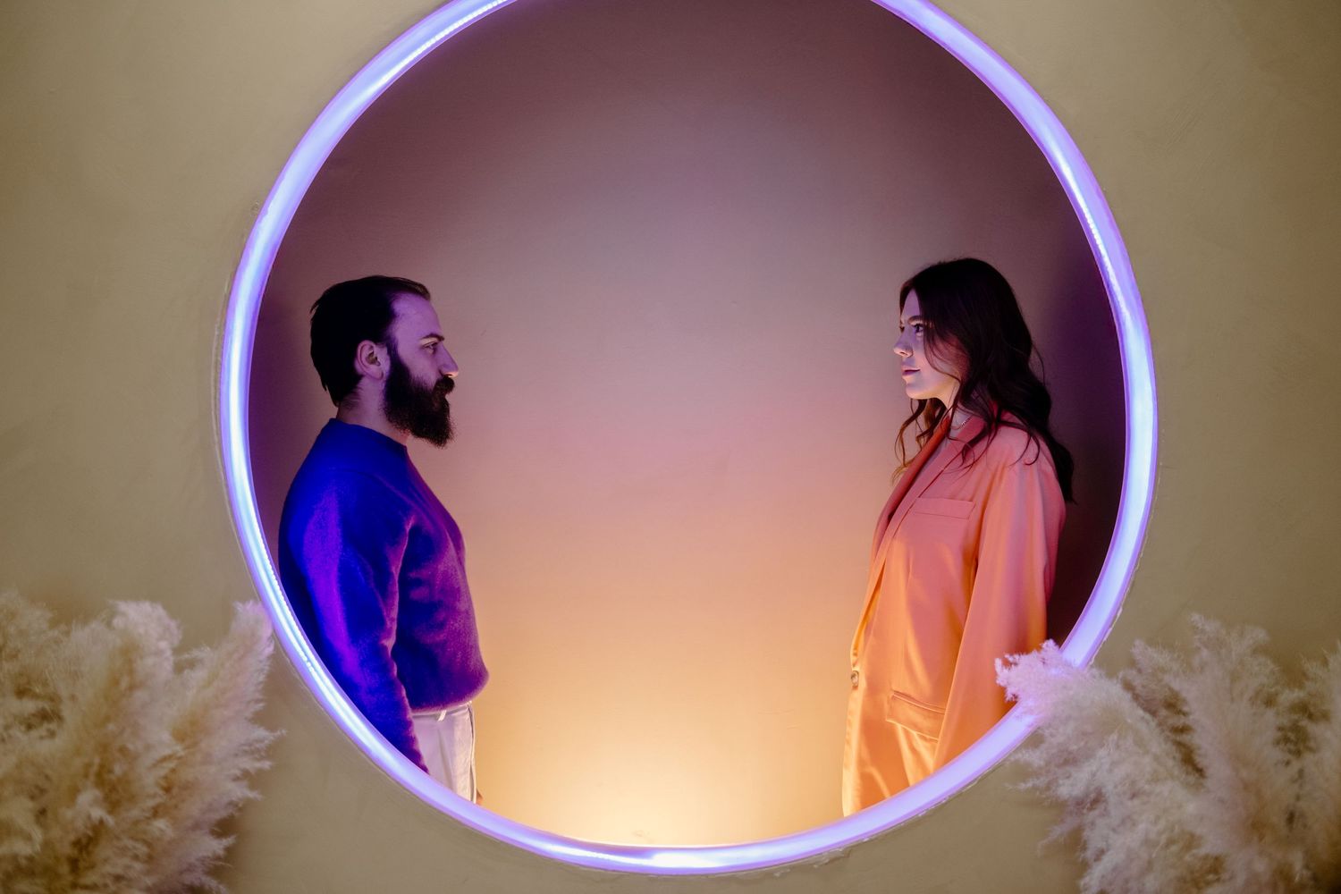 Two silhouettes face each other in a purple-lit oval frame with warm orange background lighting.