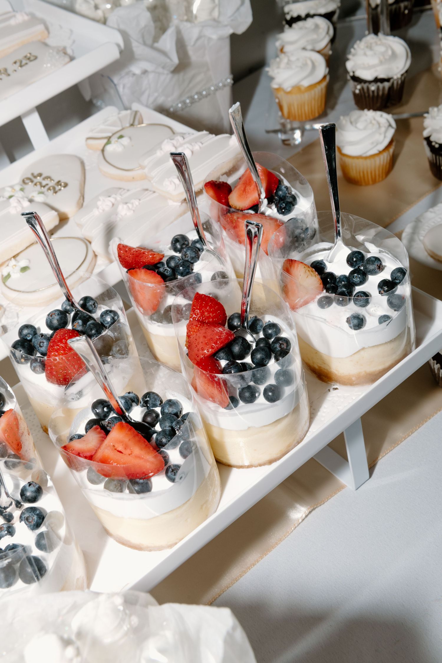 Individual dessert cups topped with whipped cream, fresh strawberries and blueberries arranged on a white serving tray.
