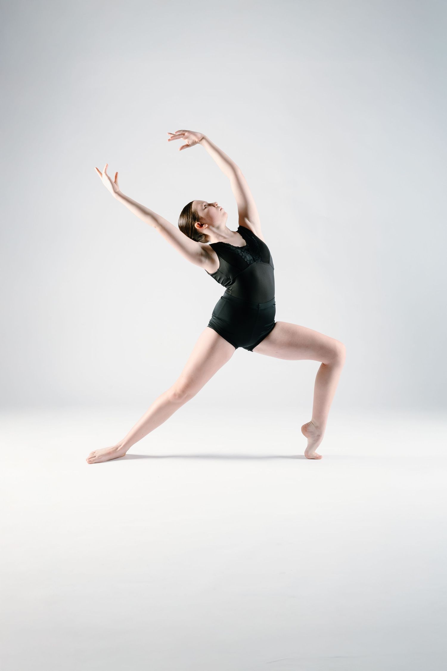 Dancer in black leotard performs graceful contemporary movement against white background.