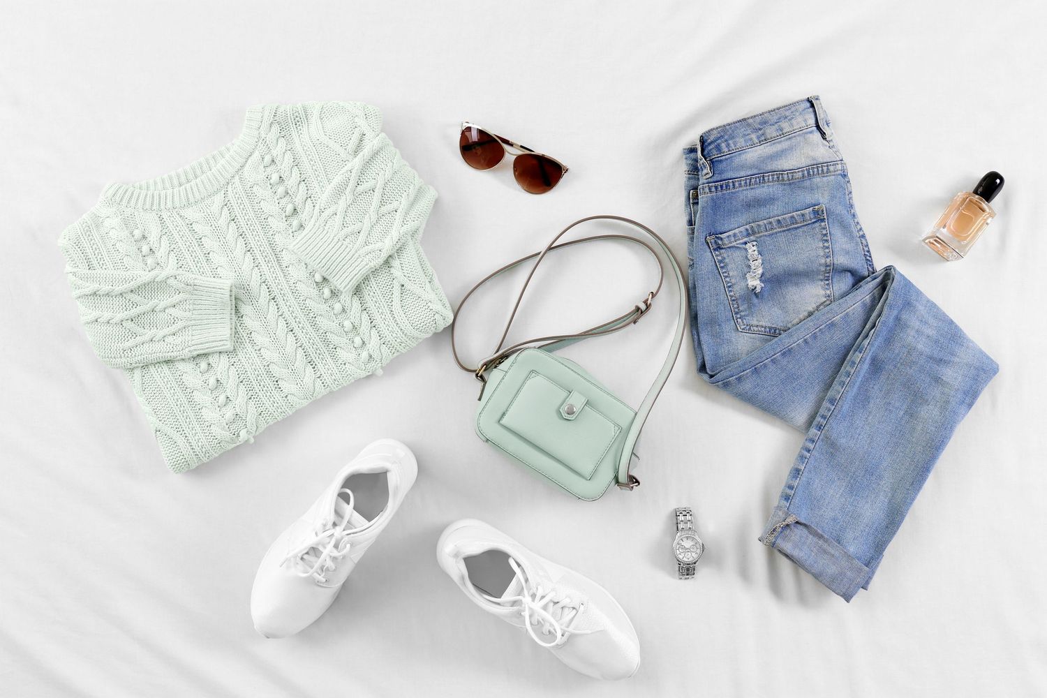 Flatlay of mint green sweater with white sneakers and light wash denim shorts on white background.