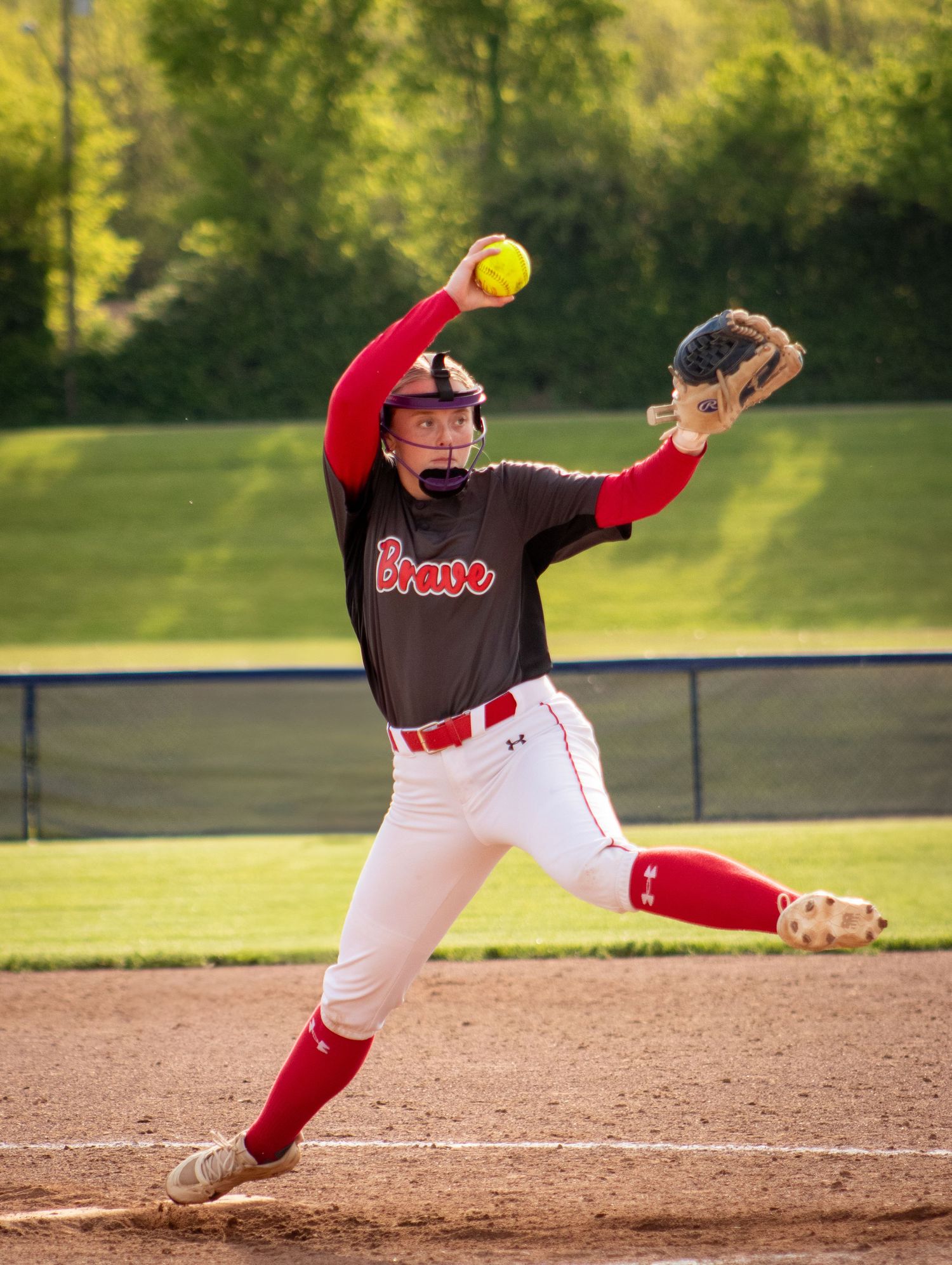 A softball player in red and brown uniform makes a diving catch attempt on the field during a game.