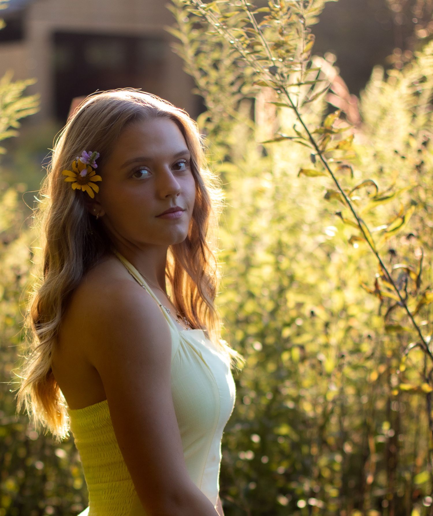 A girl in a yellow dress poses thoughtfully against a sunlit natural backdrop with golden bokeh effects.