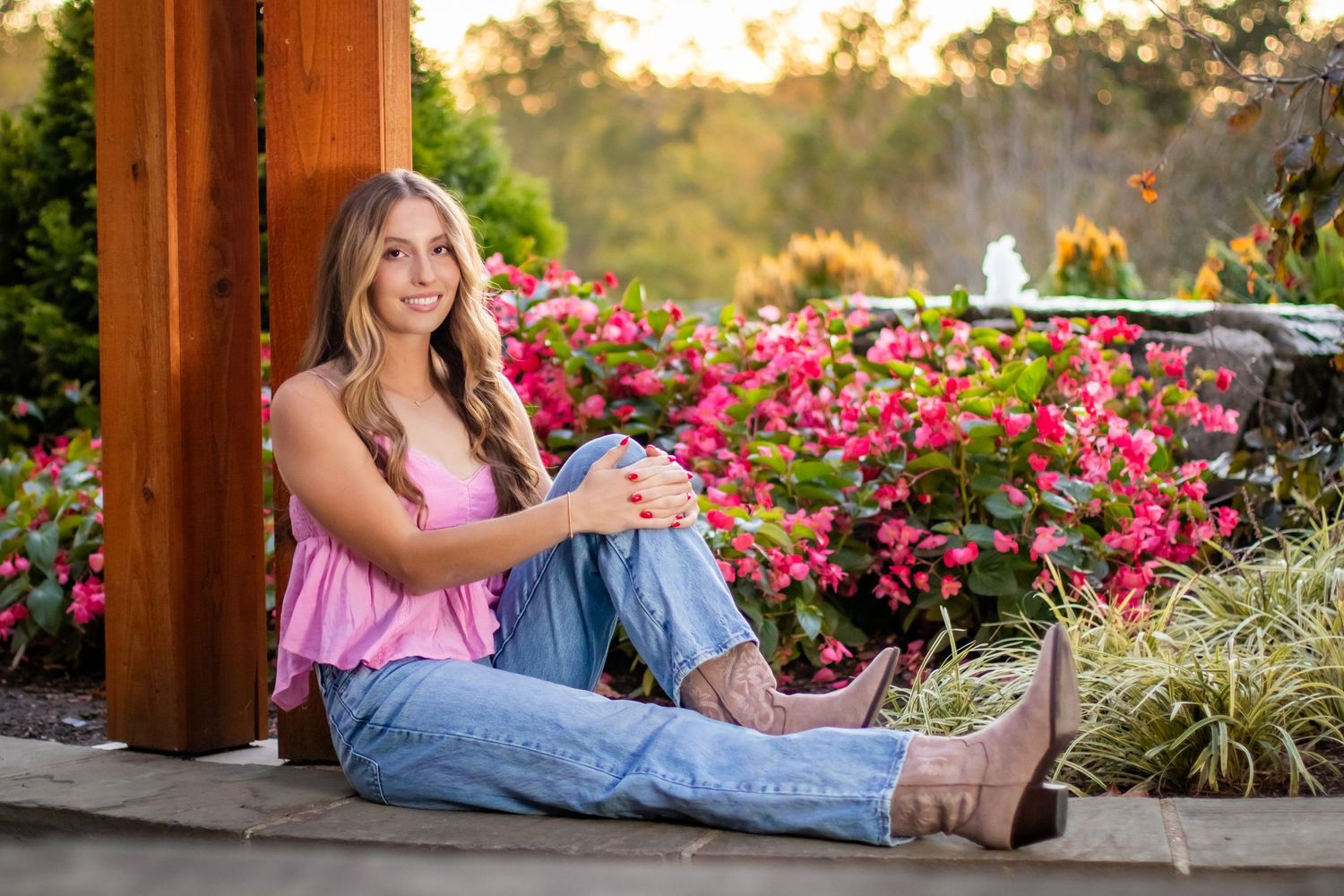 A person in casual attire relaxes on a wooden deck surrounded by vibrant pink flowers during golden hour.