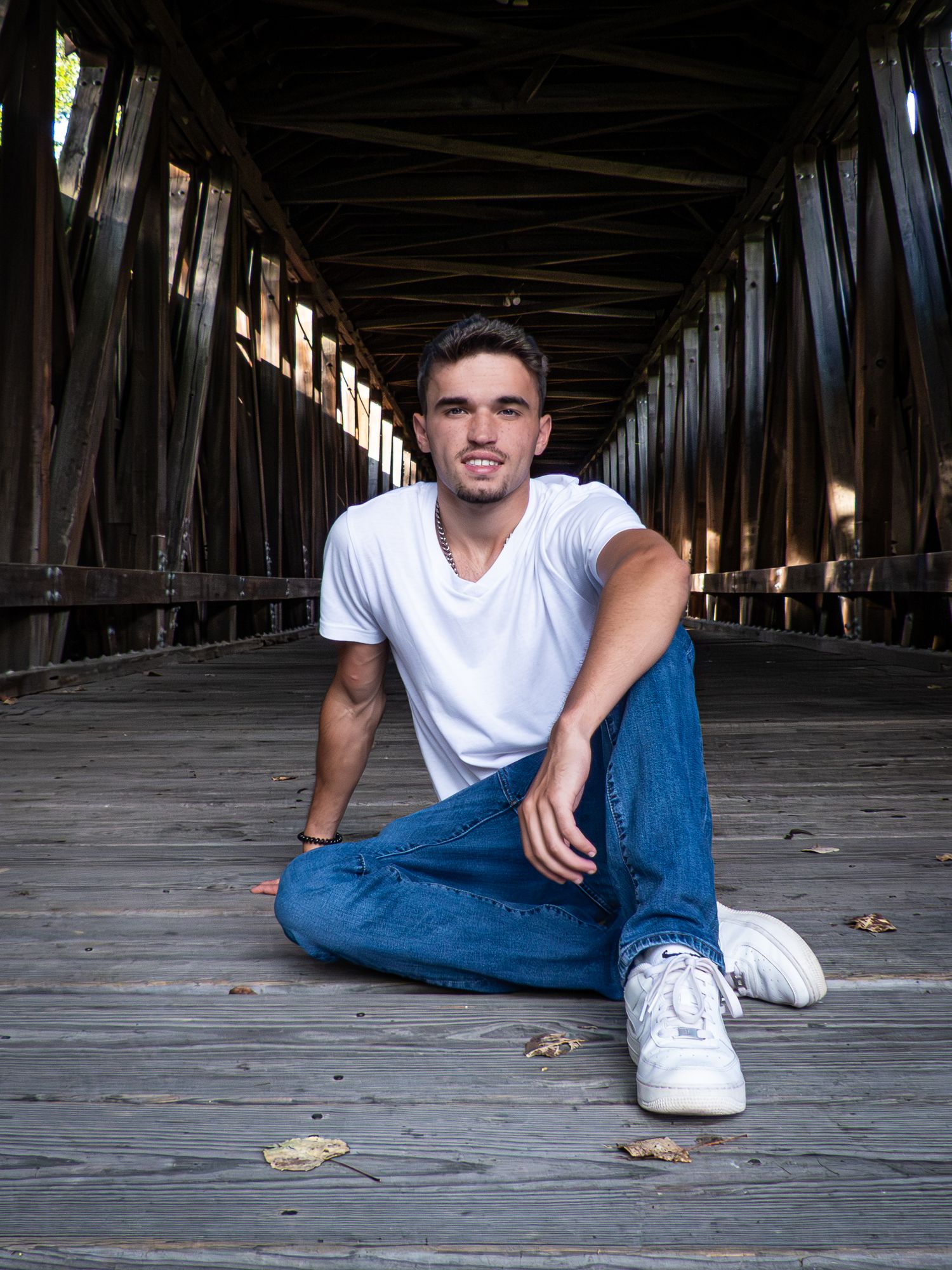 Portrait of person sitting on wooden covered bridge wearing white t-shirt and jeans.