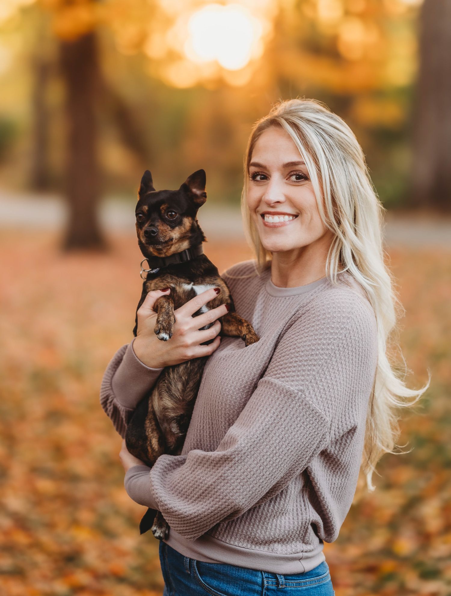 Autumn portraits with a small black dog being held while wearing a cozy sweater.