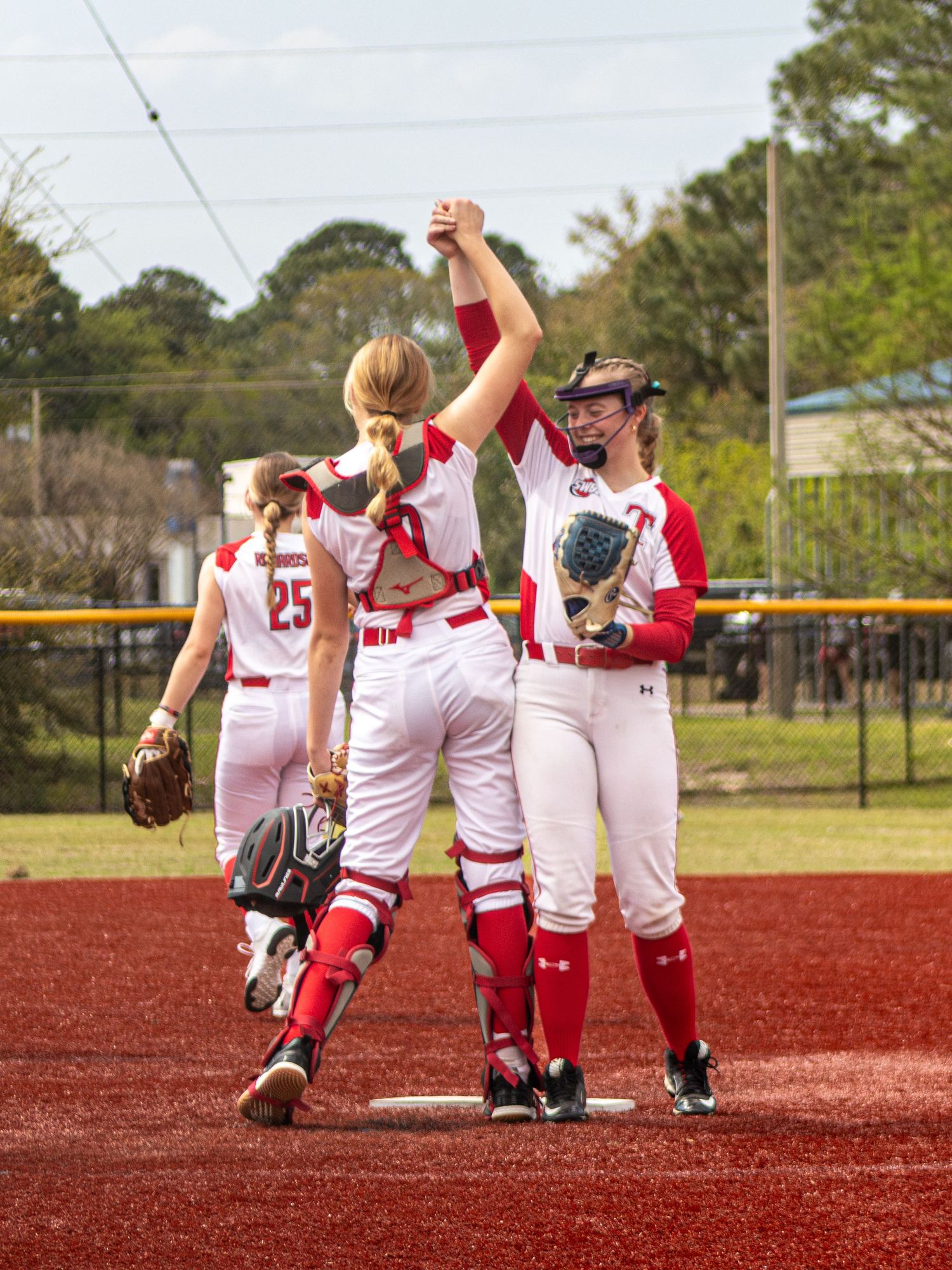 Baseball players in red and white uniforms huddle together on a red dirt field during a game celebration.