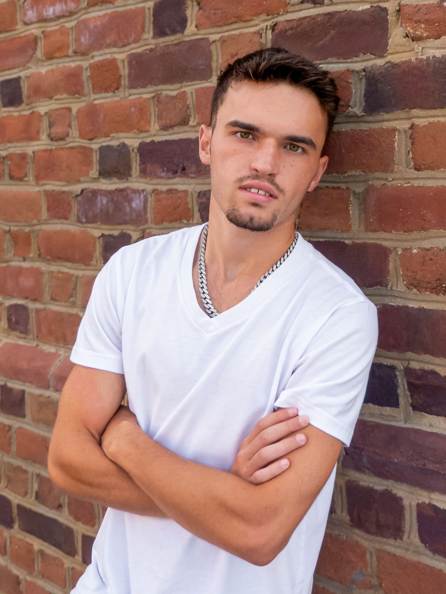 Portrait against brick wall wearing white t-shirt and silver chain necklace.