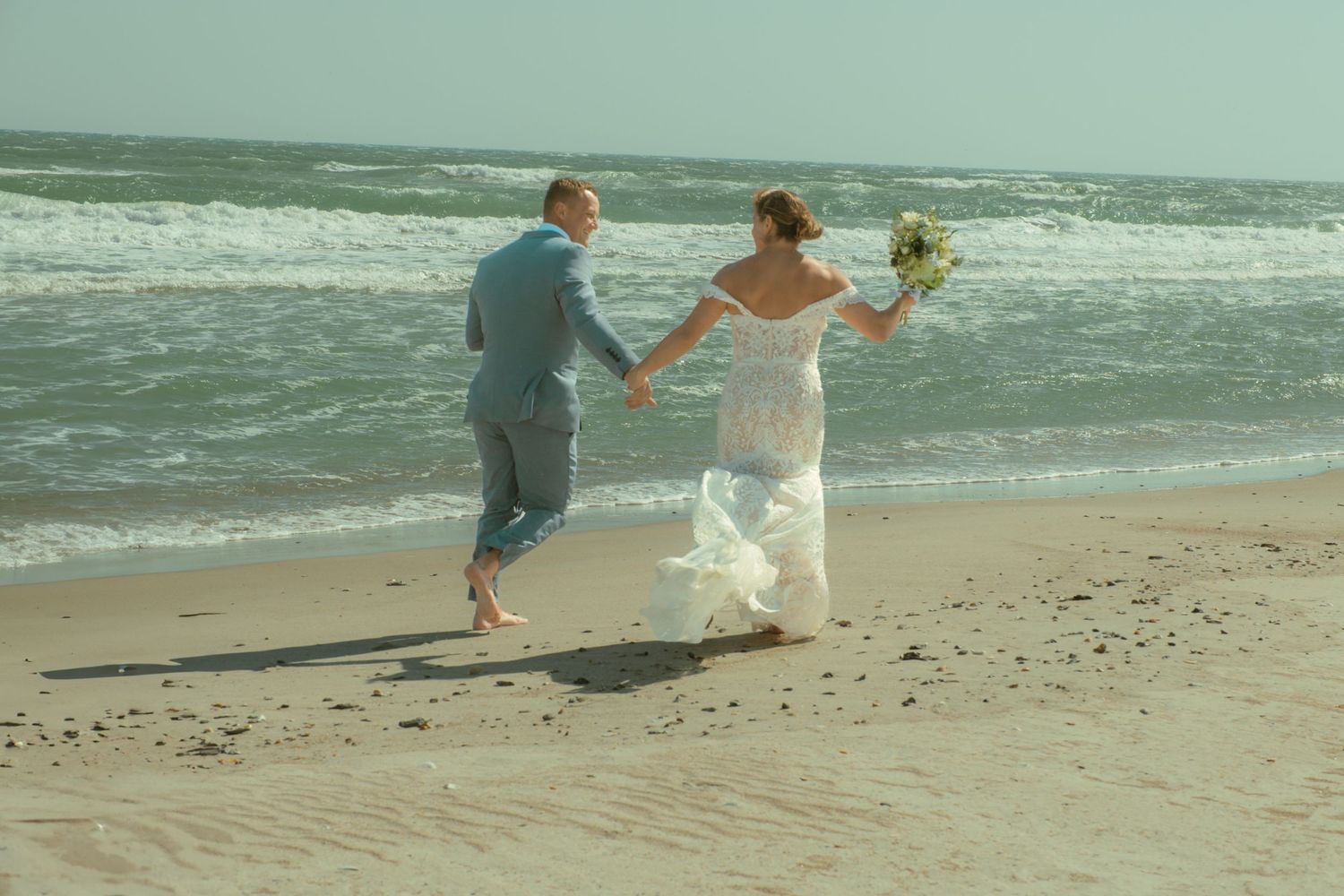 Joyful newlyweds leap and dance together on a sunny beach. Alex Faye Photography Alex Faye Media Wedding Photographer Raleigh