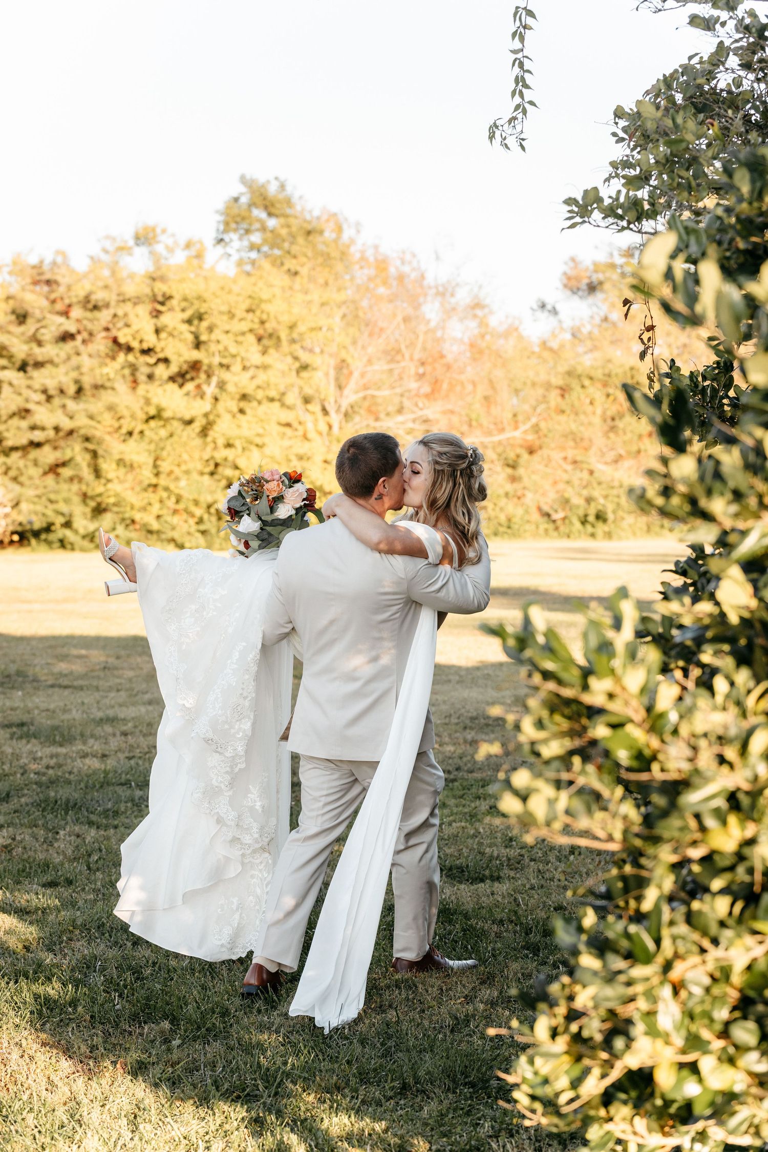 Couple in white attire sitting together on grassy field during golden hour. Alex Faye Photography Alex Faye Media Wedding Raleigh