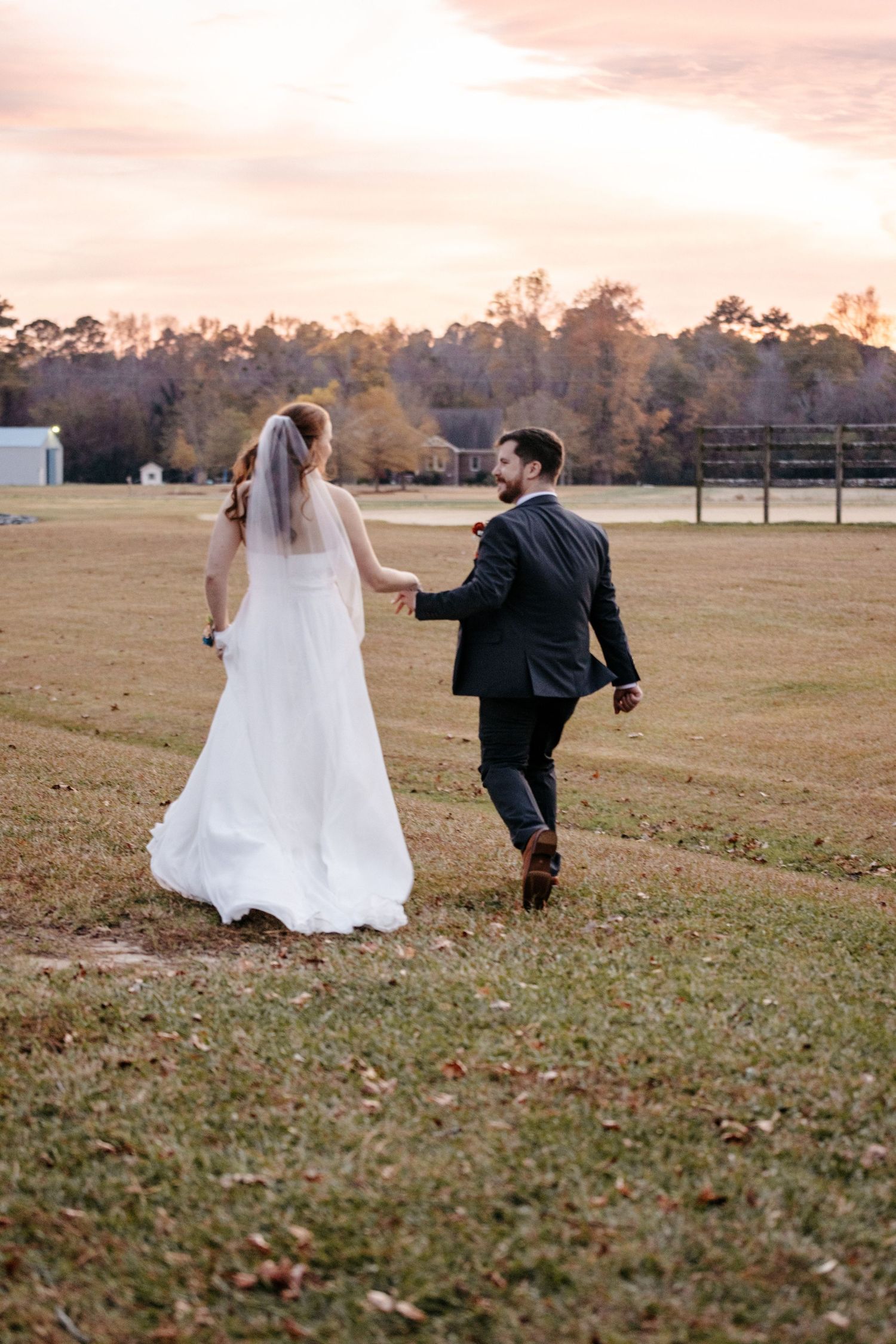 Couple walking hand in hand across field during sunset after wedding ceremony. Alex Faye Photography Alex Faye Media Wedding Raleigh