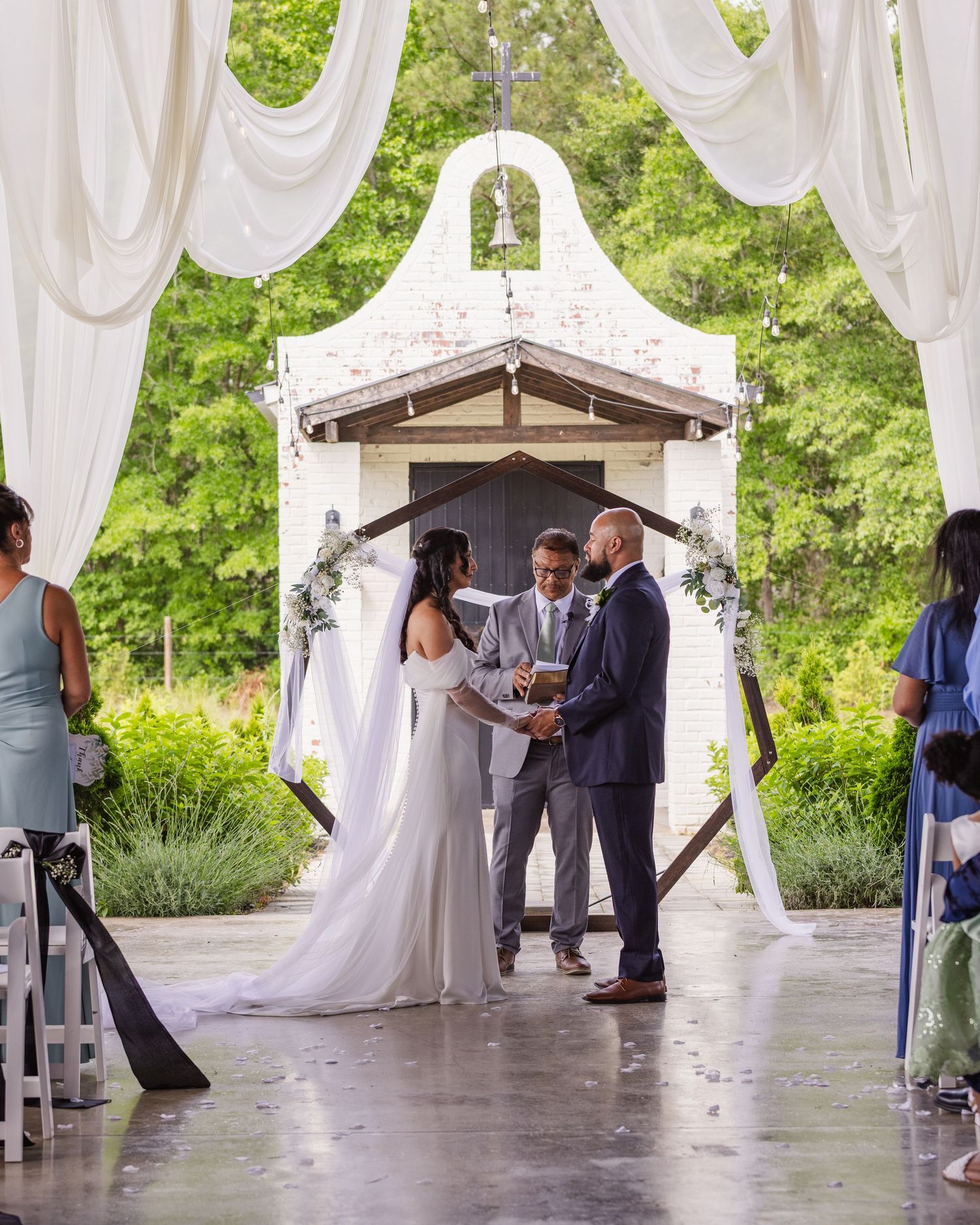 Bride and groom exchange vows outdoors under white draped canopy at elegant garden wedding ceremony.