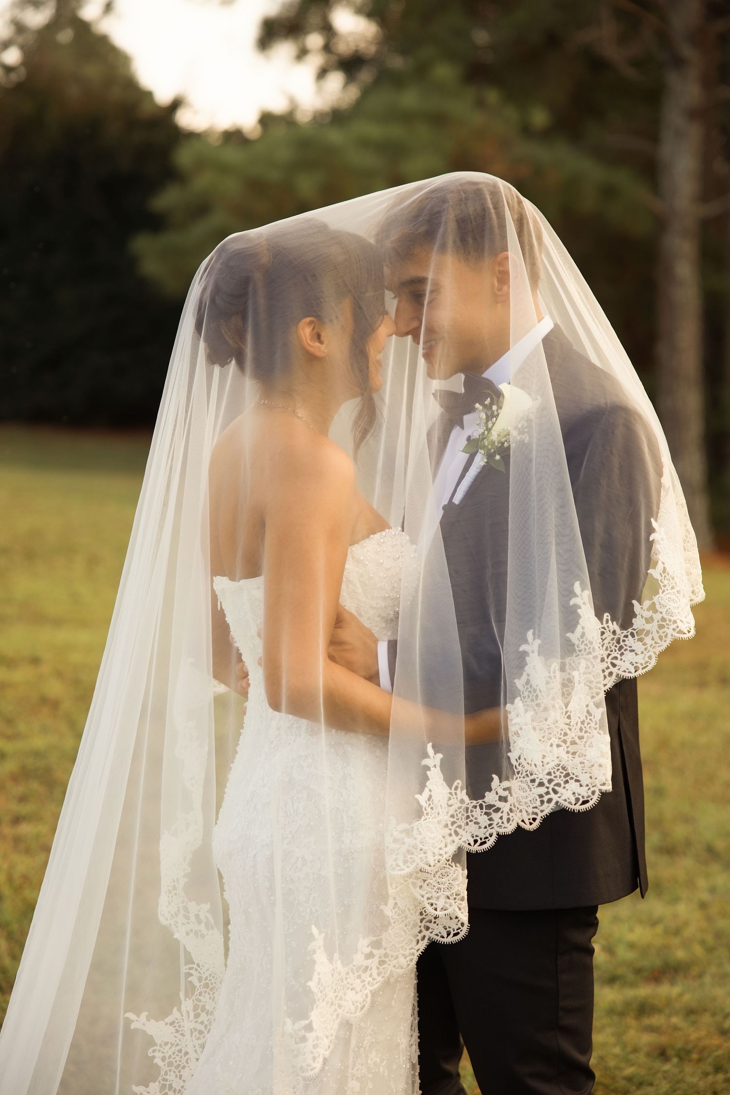 A romantic wedding moment captured through delicate lace veil in an outdoor garden setting at sunset. Alex Faye Photography Alex Faye Media