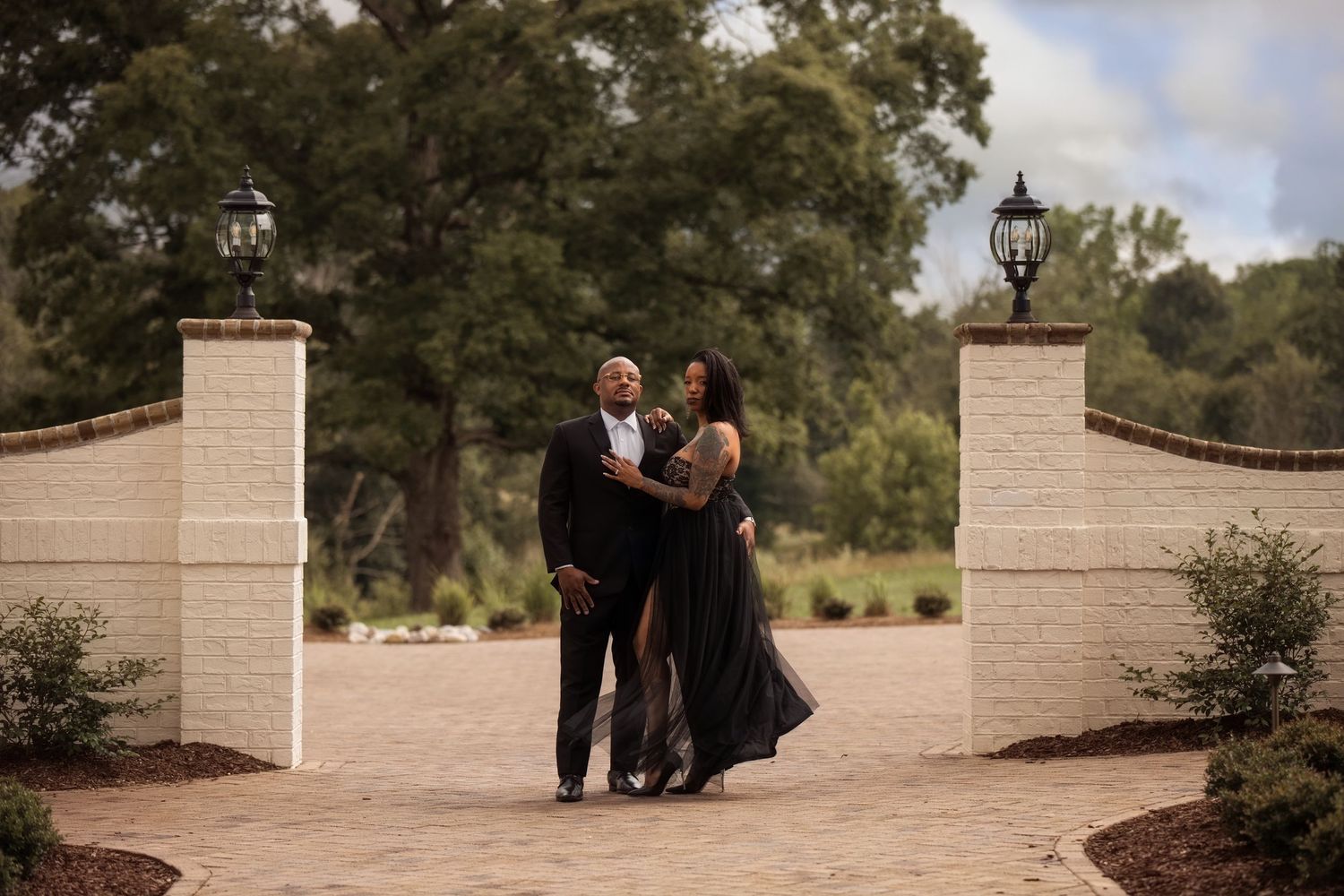 Romantic couple poses between stone pillars at an elegant outdoor venue. Alex Faye Photography Alex Faye Media Wedding Photographer Raleigh