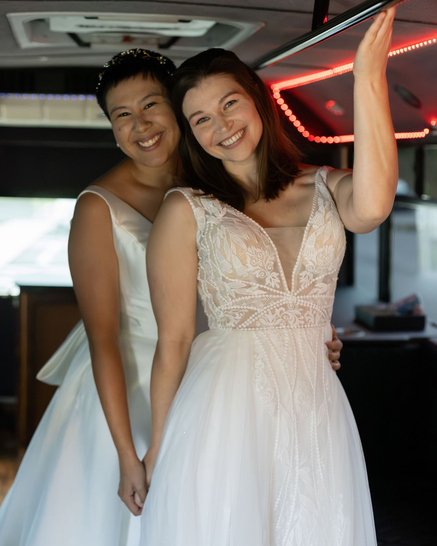 Two brides in white wedding gowns smiling and holding hands at their wedding reception.