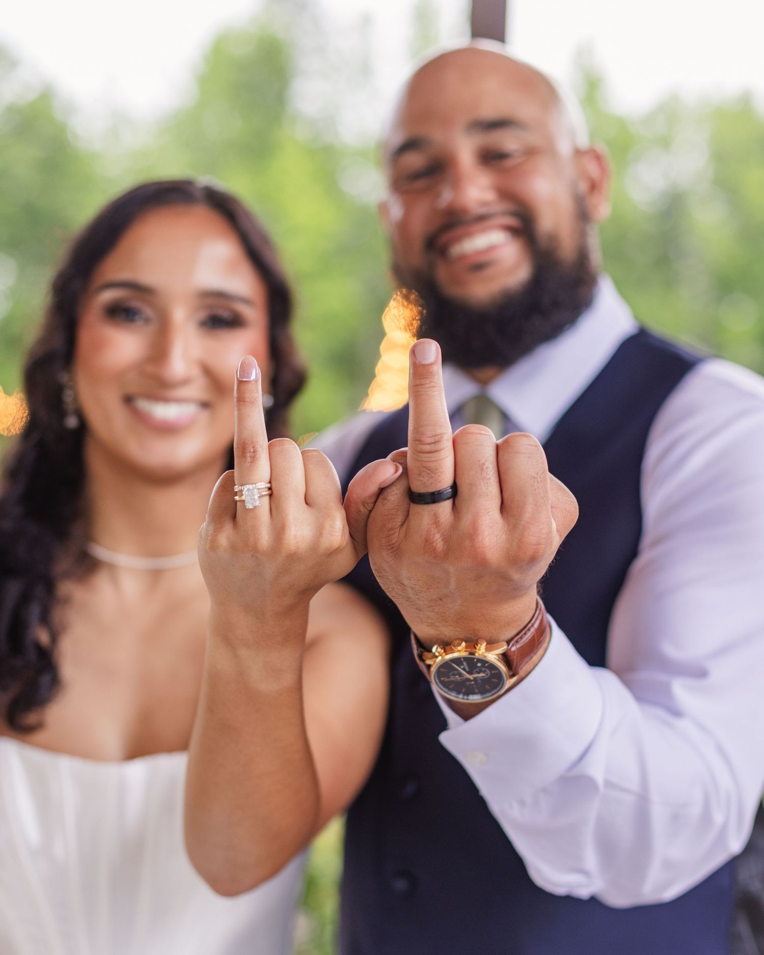 Newlywed couple smiling and showing off their wedding rings on their ring fingers at their wedding ceremony.