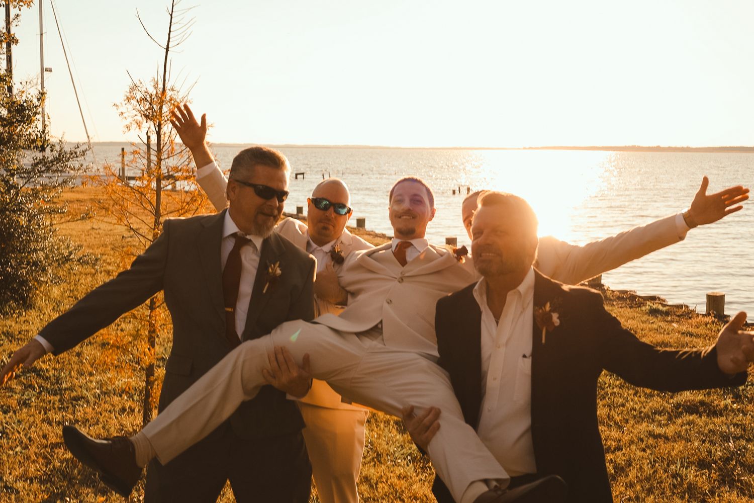 Wedding party members jumping and celebrating together at golden hour by the water. Alex Faye Photography Alex Faye Media Wedding Raleigh