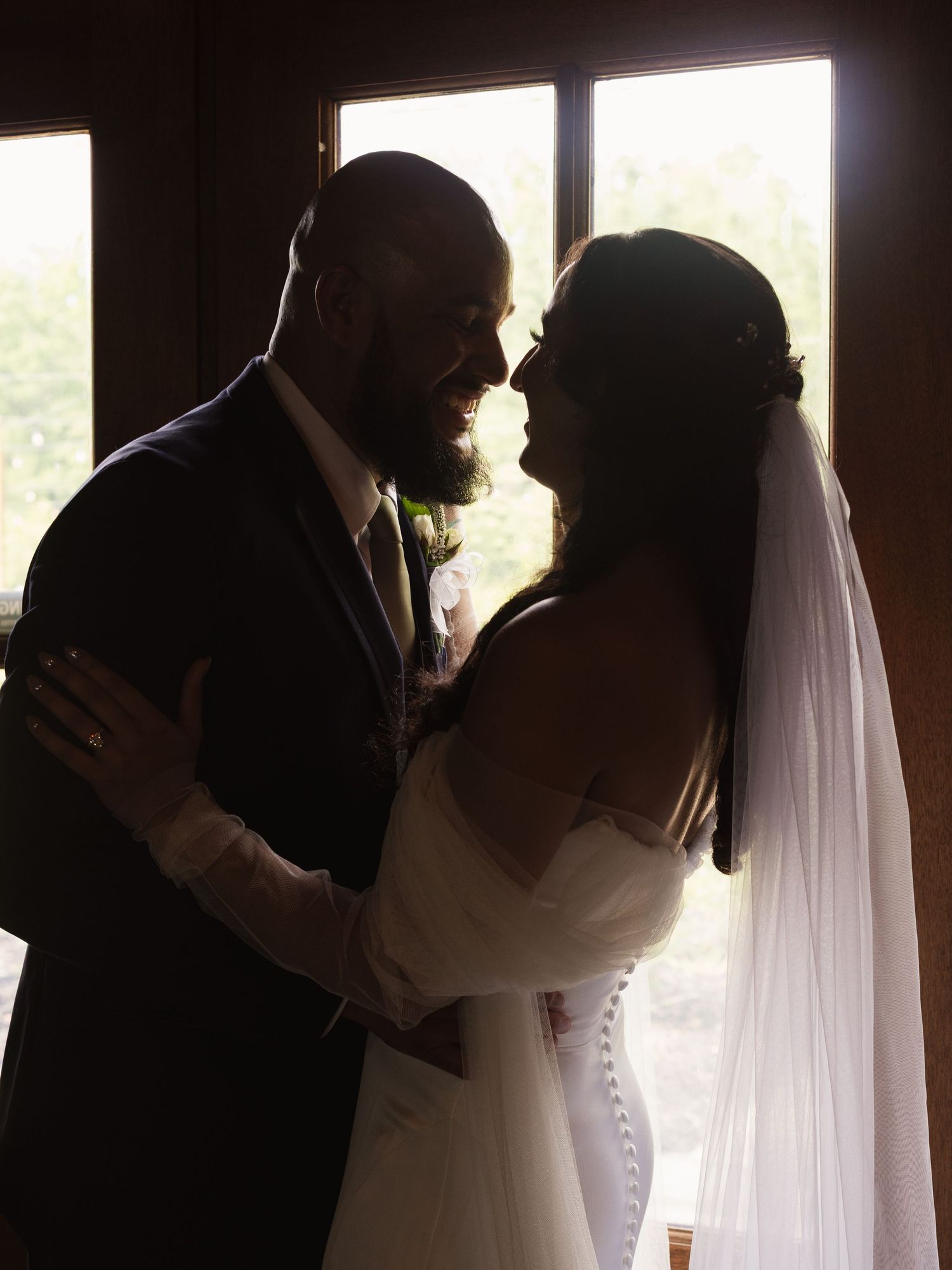 Silhouette of bride and groom embracing near window in romantic wedding portrait.