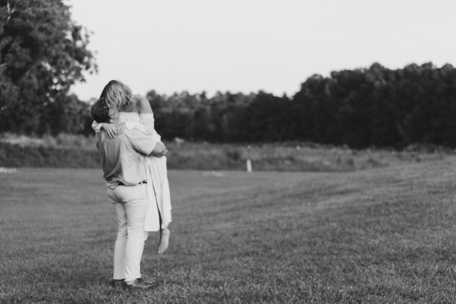 A romantic black and white photo of a couple embracing in an open field at sunset. Alex Faye Photography Alex Faye Media Wedding Raleigh