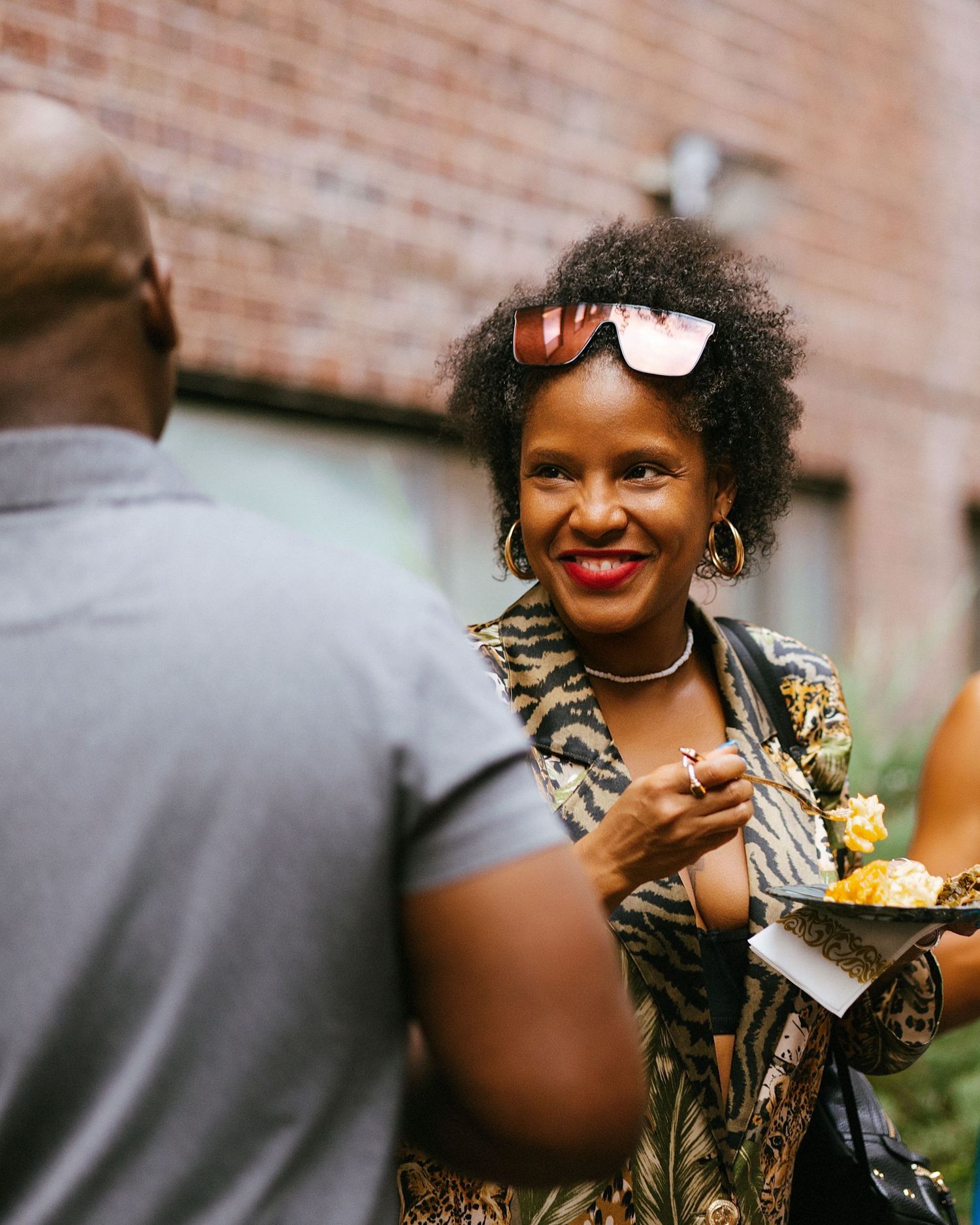 Person in an animal print dress smiling and laughing during an outdoor gathering.