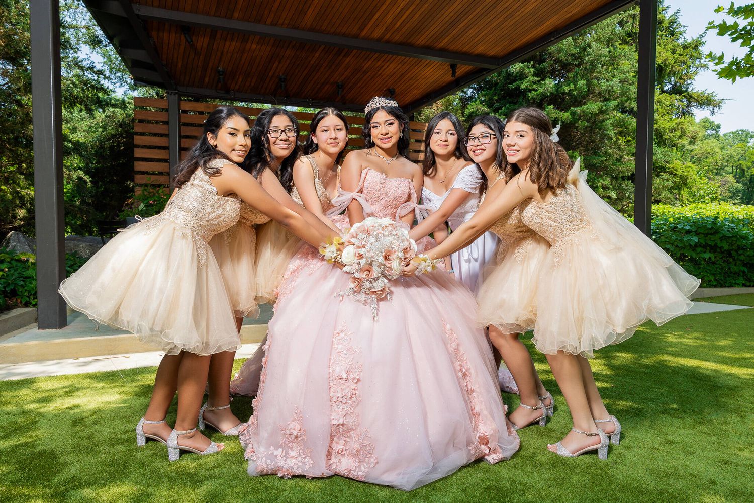 Bridesmaids in champagne dresses pose with bride in pink gown during outdoor garden wedding photoshoot.
